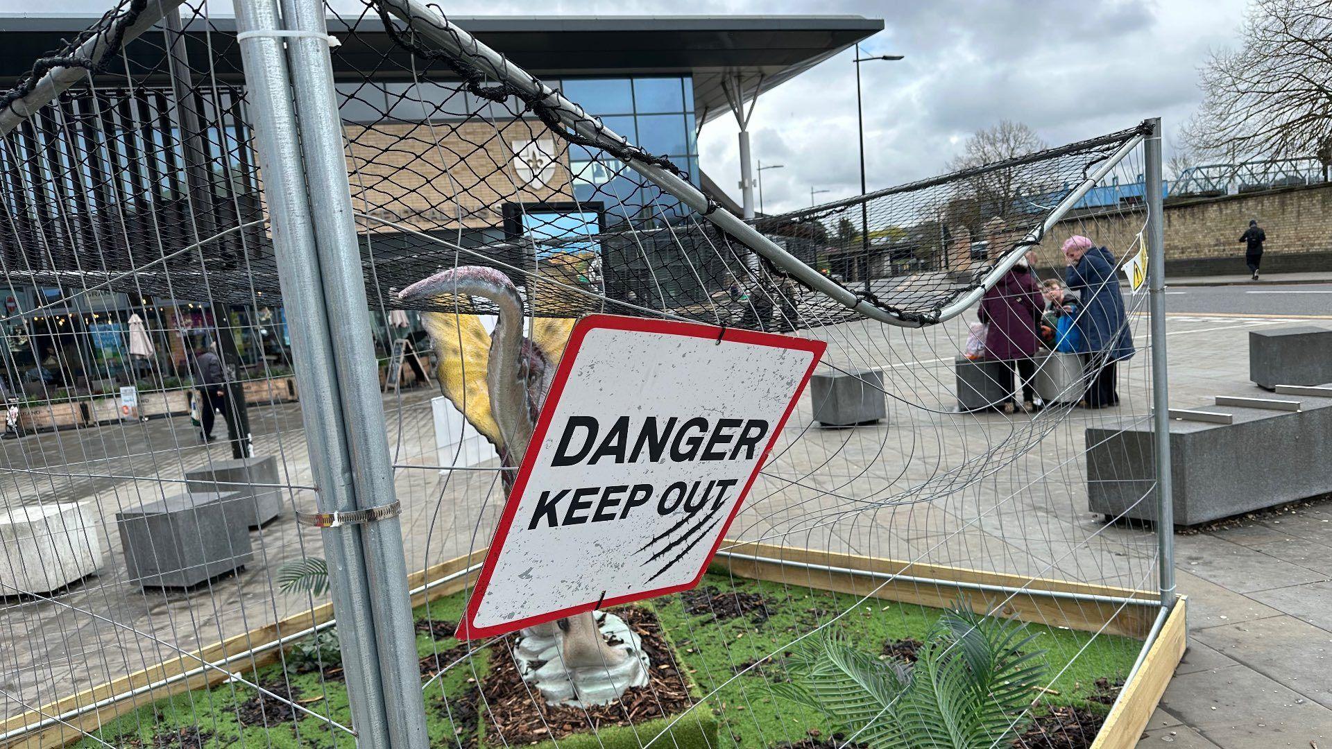 A damaged cage containing a dinosaur sculpture