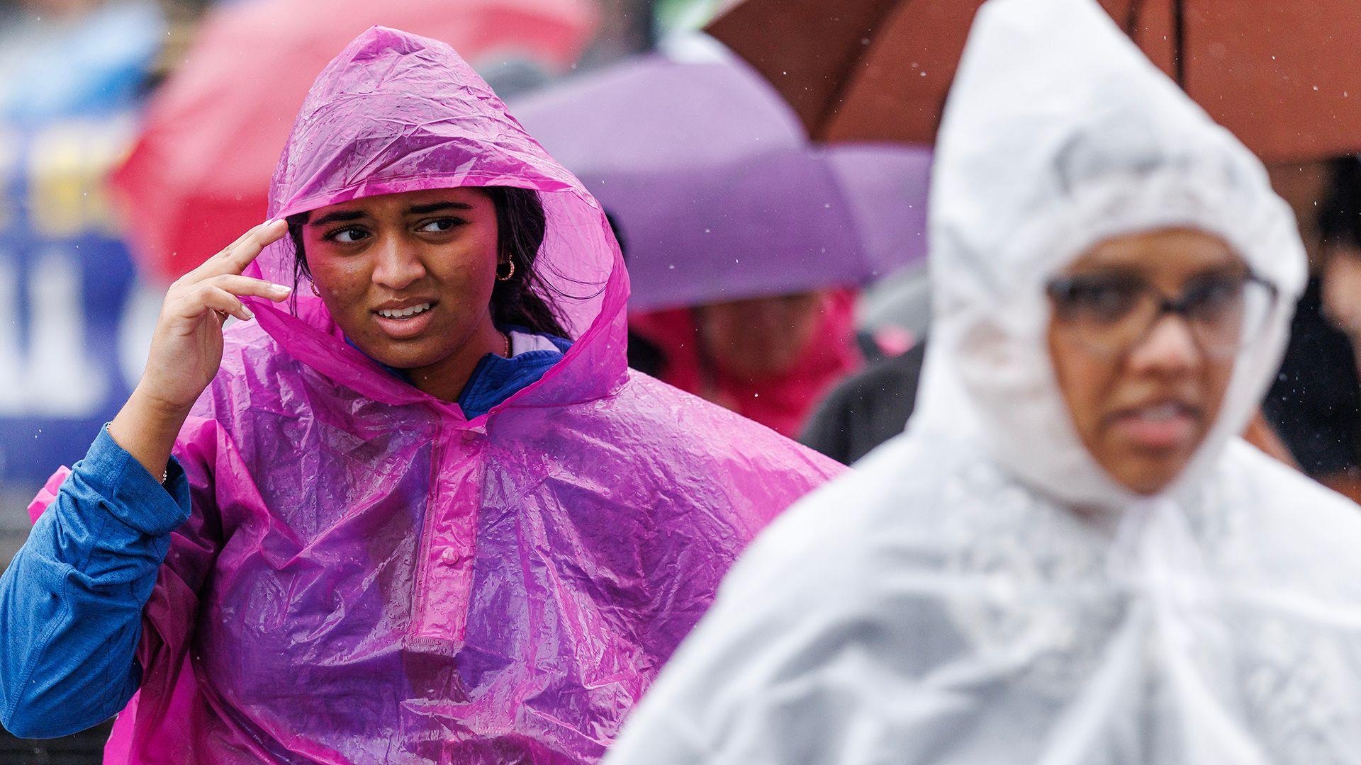 Two people are pictured walking on a street wearing plastic overcoats during a rain shower, on Westminster Bridge in London in June.