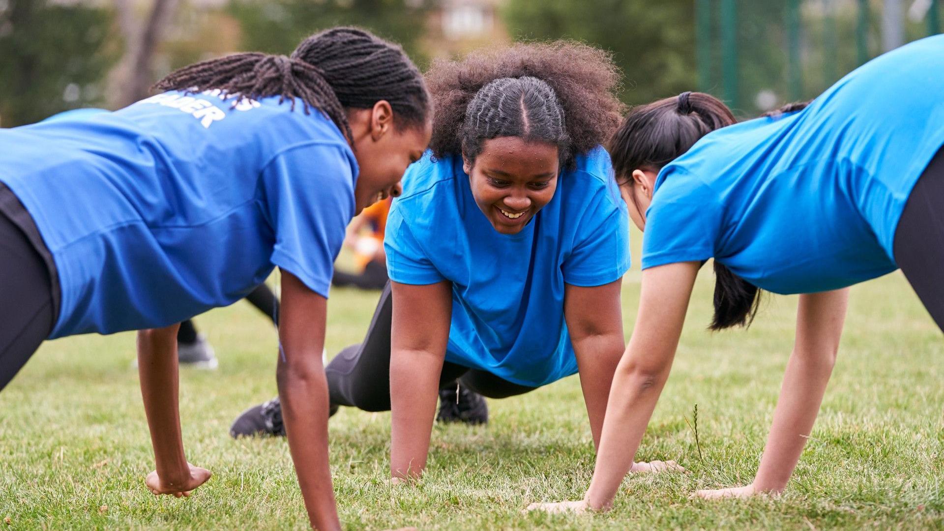 Three girls smile as they exercise in a park
