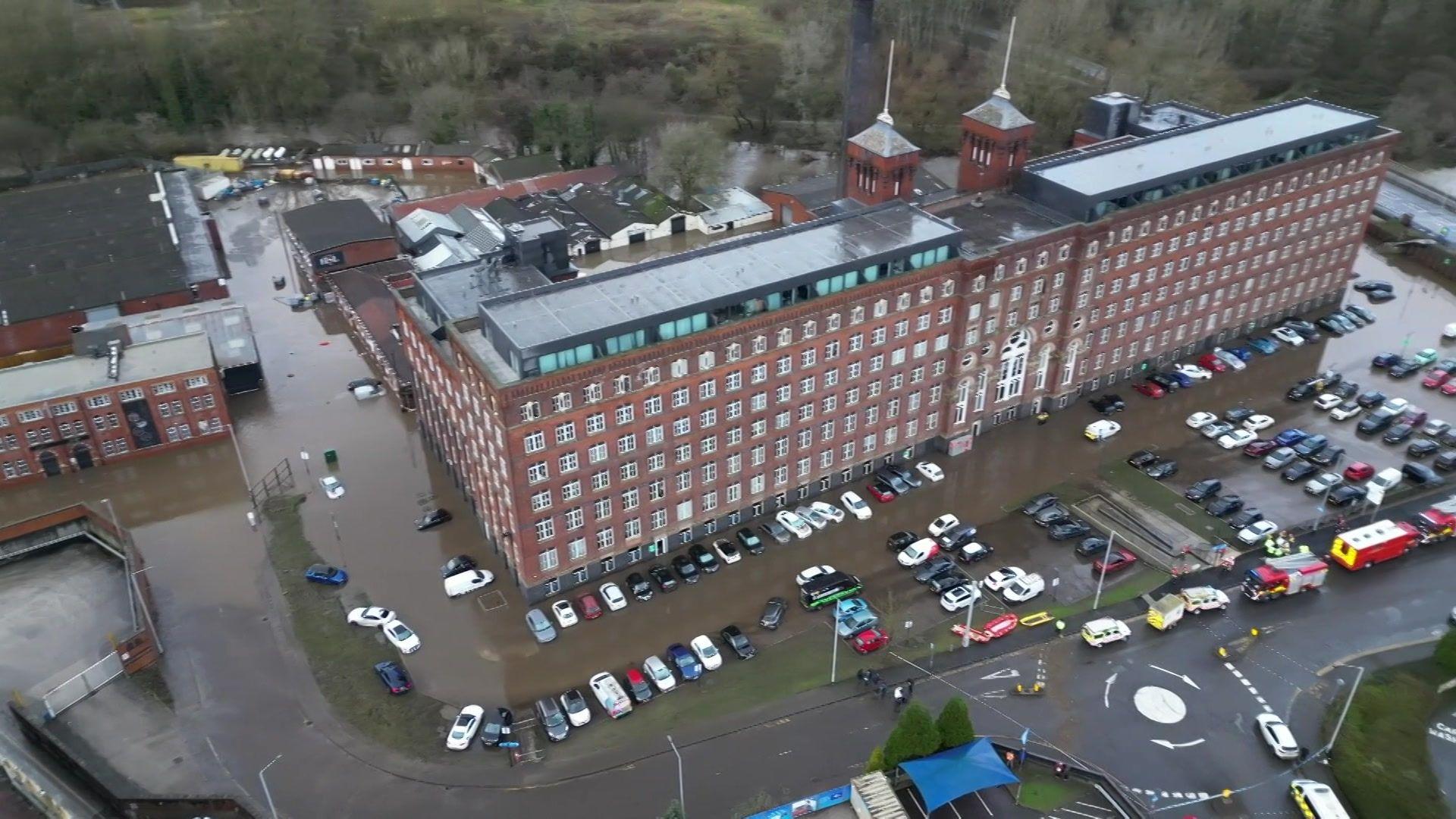 An aerial shot of a large converted mill surrounded by flood water and with fire engines outside 