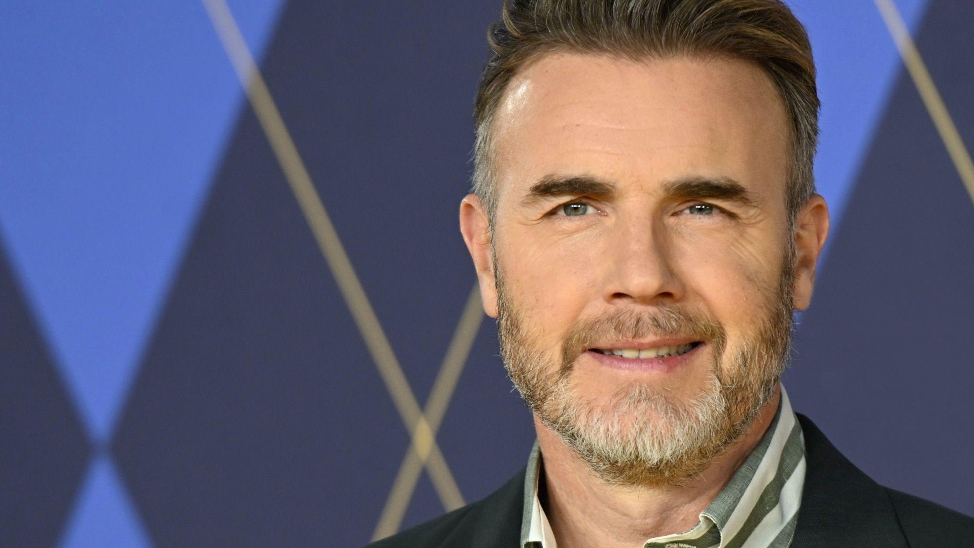 Gary Barlow looking towards the camera and smiling.