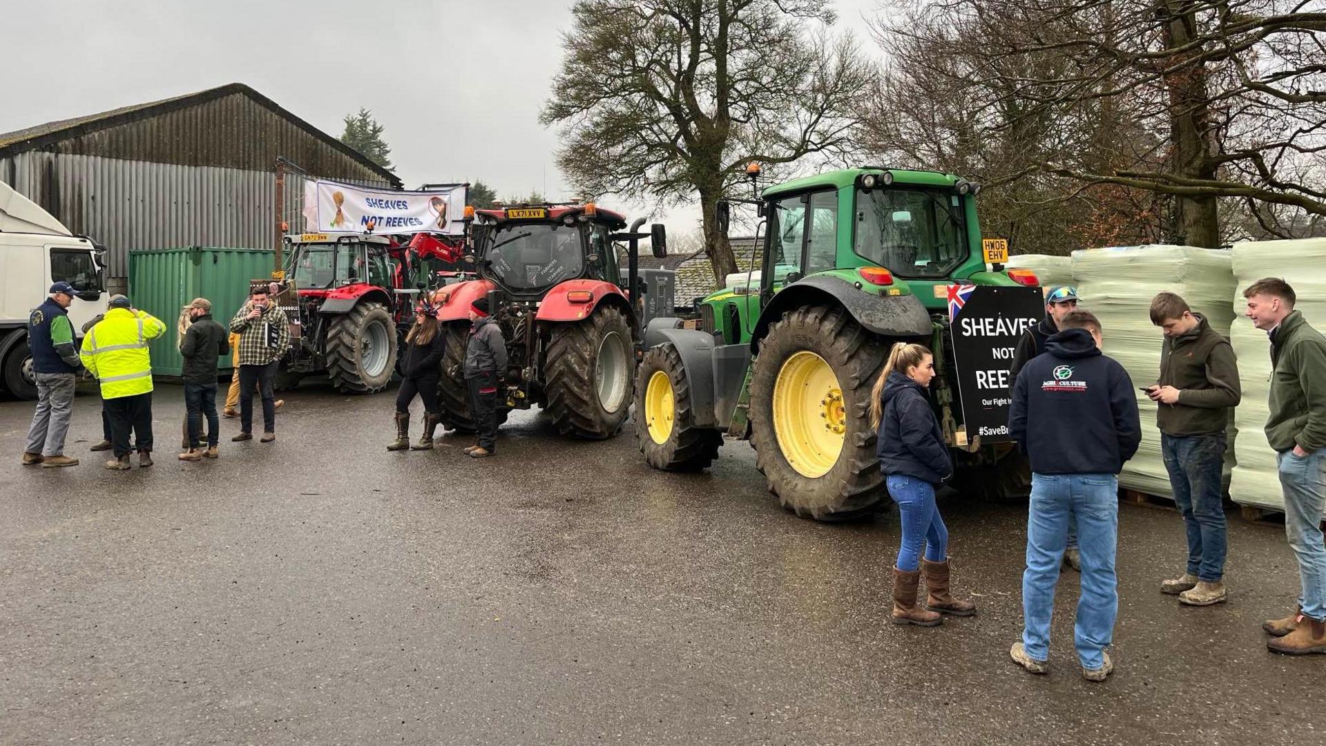 A group of people standing by tractors, some have protest signs on them.