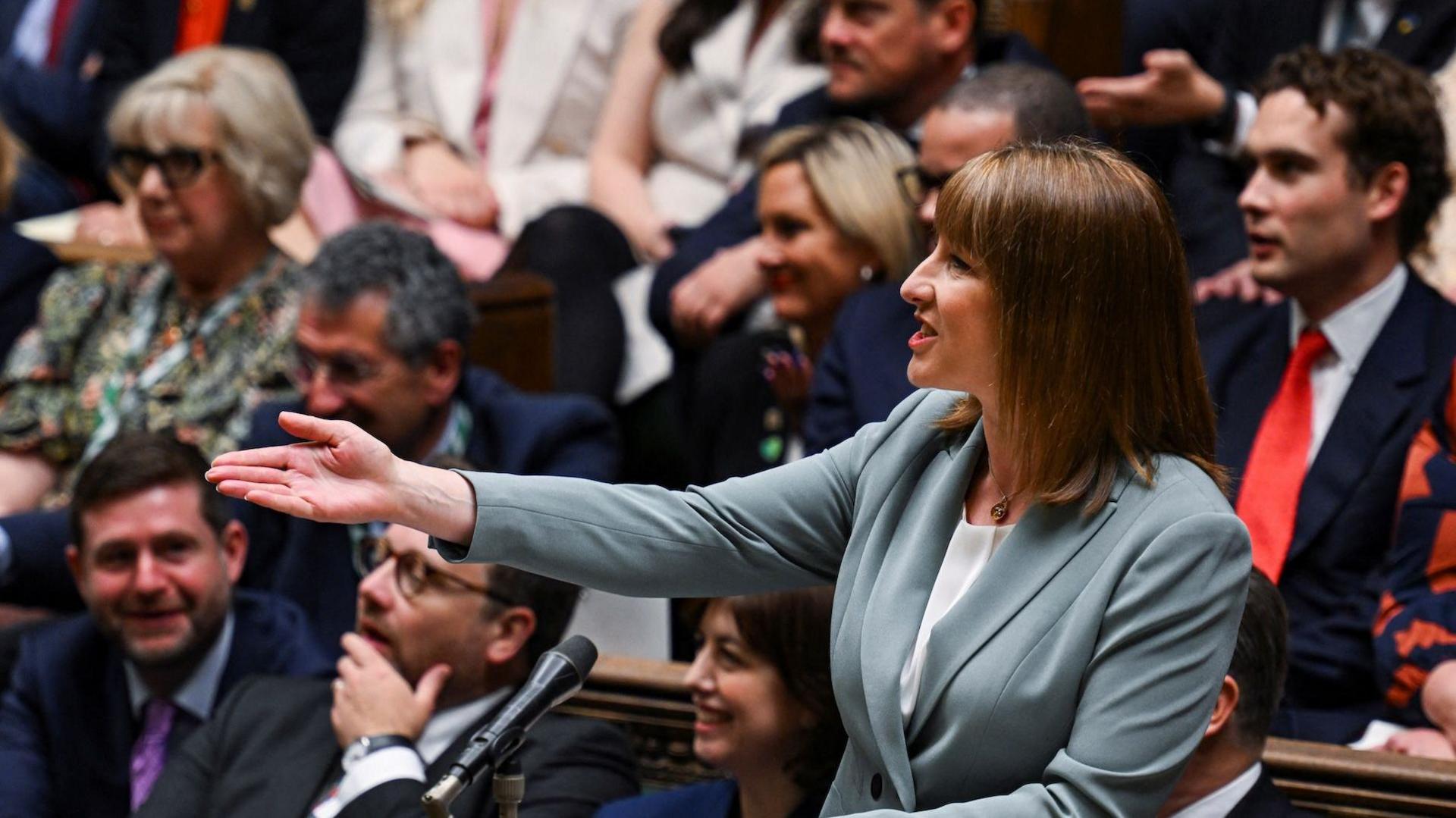 Chancellor Rachel Reeves stands in the House of Commons during her Spending Review speech in 2025. She is wearing a turquoise jacket and white top - she has her right hand out gesturing to the other side of the house and is mid speech.