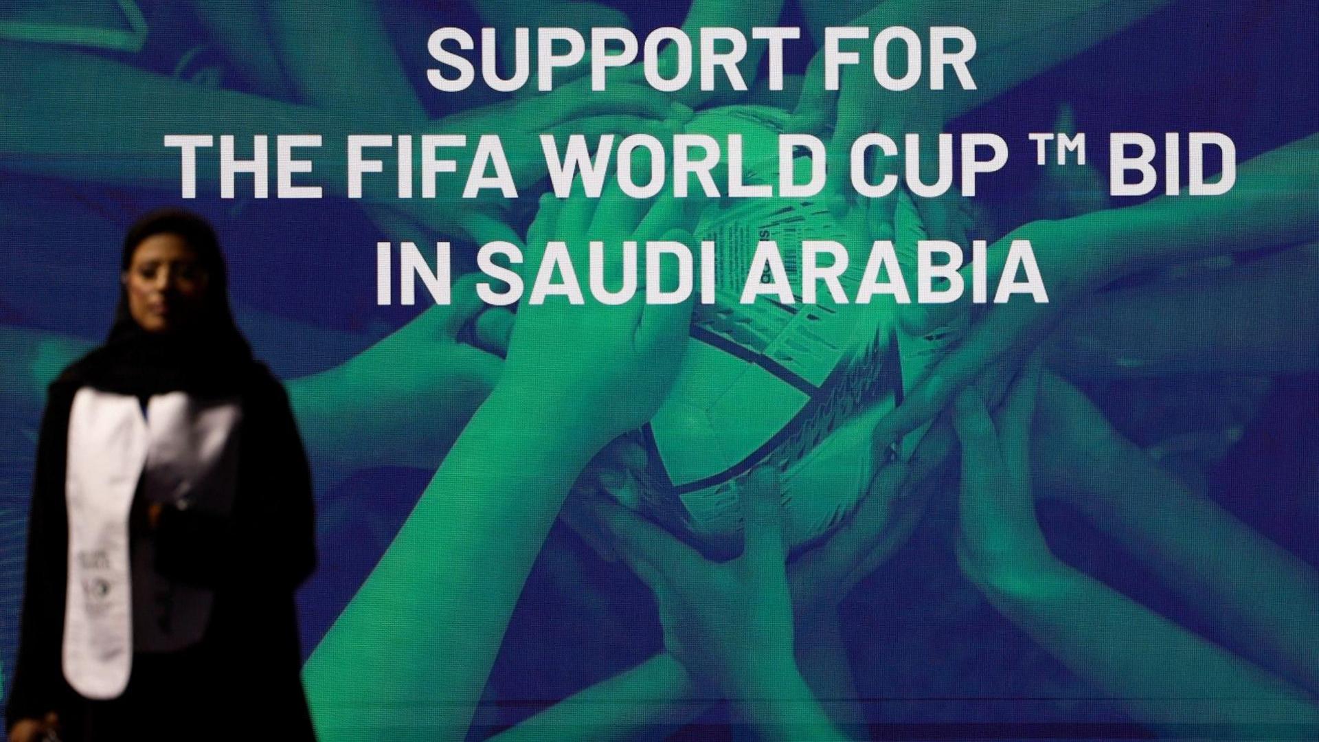 A woman stands in front of a 'support for the Fifa World Cup bid in Saudi Arabia' 