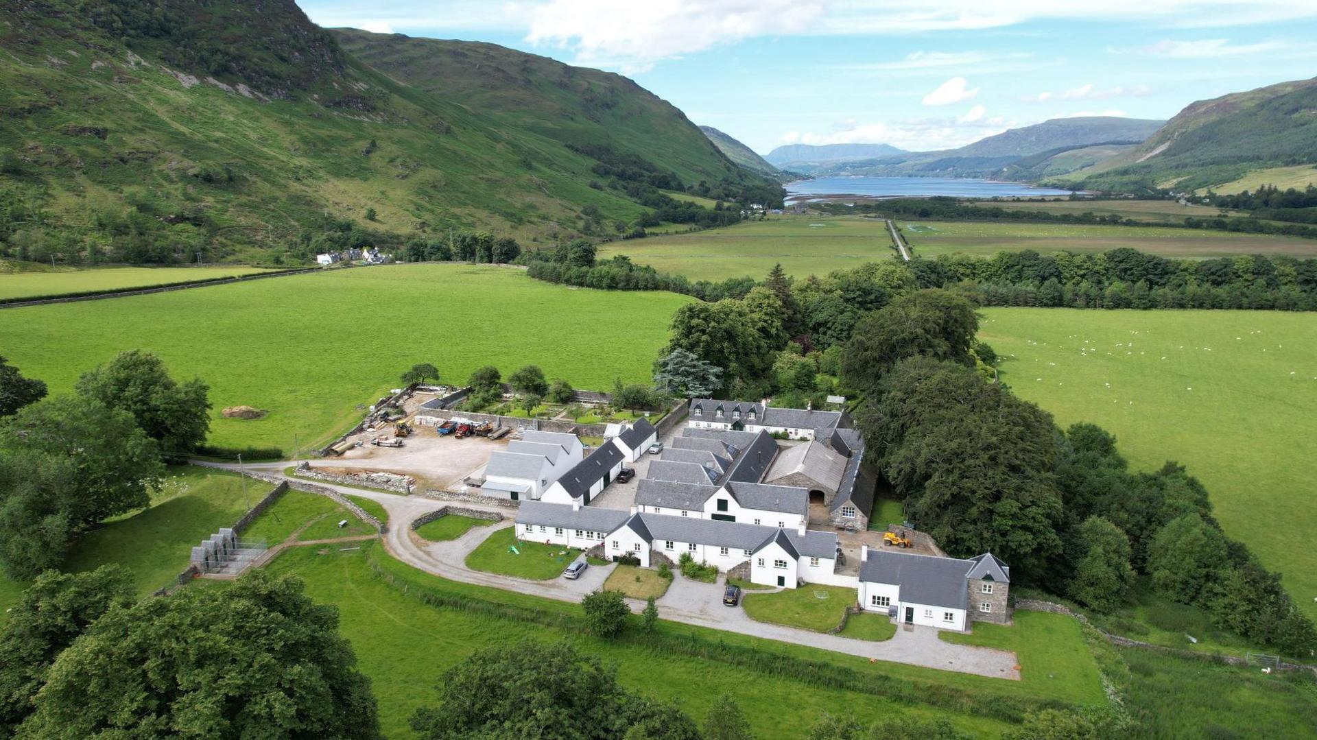 The farm is large with several white-walled buildings and houses. The property is on the floor of a glen.