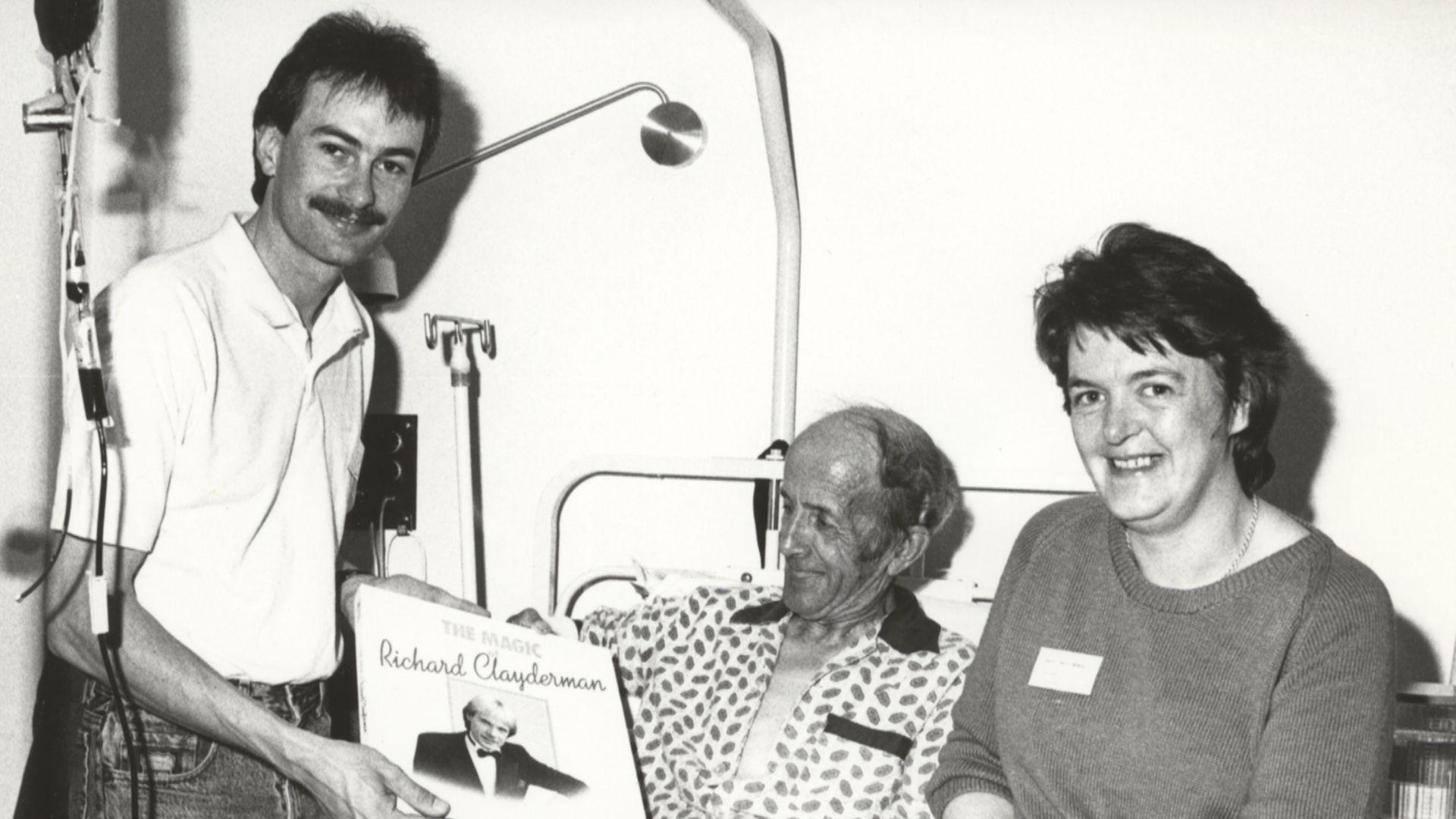 Dau berson yn ymweld a chlaf yn yr ysbyty