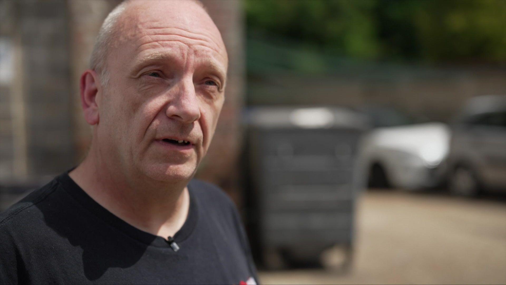 Neil wearing a black top and stood in front of some cars