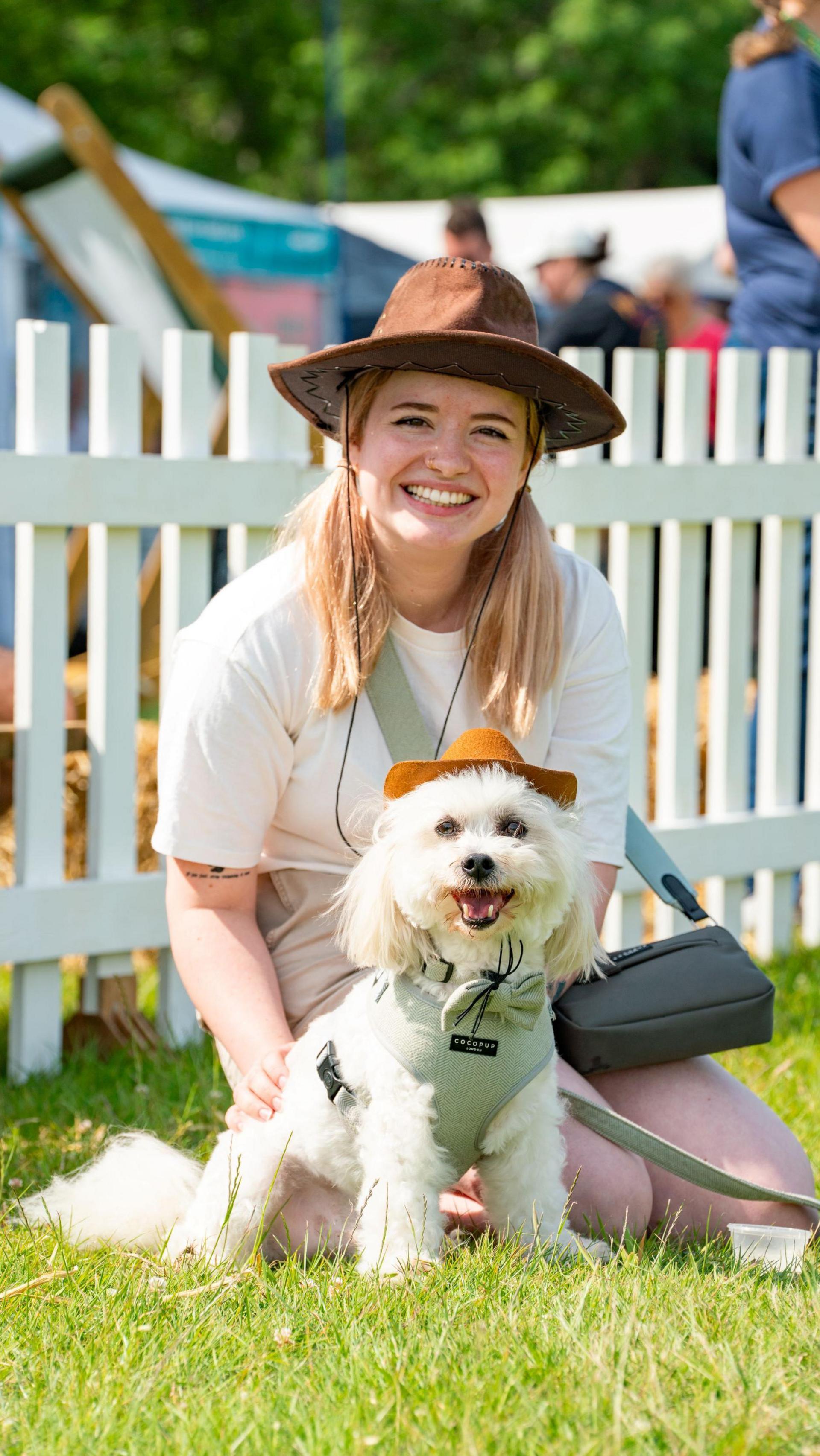 a woman knelt with her dog and both are wearing cowboy style hats. 