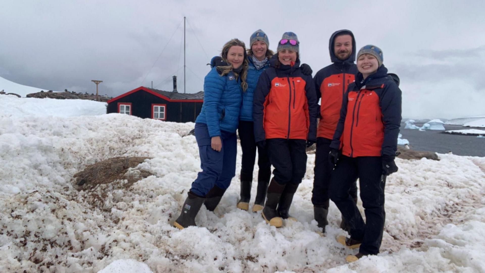 A picture of Dale Ellis wth her four other teams mates in Port Lockroy. They are dressed in outdoor weather clothing and are stood together smiling in the snow. 