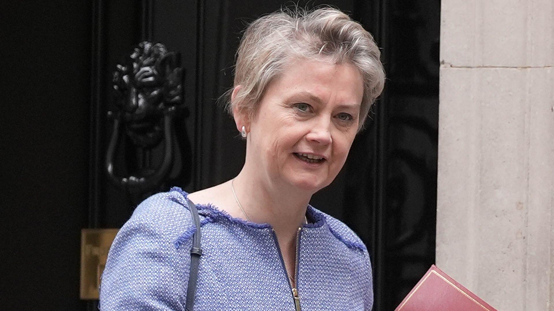 Home Secretary Yvette Cooper looks towards the camera while wearing a blue top with cropped short hair outside Number 10 Downing Street, holding a red file just in view, in London in July.