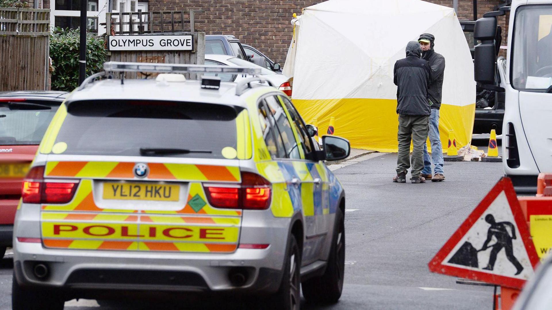 The scene of the shooting with a police car and crime tent, and a road sign that says Olympus Grove