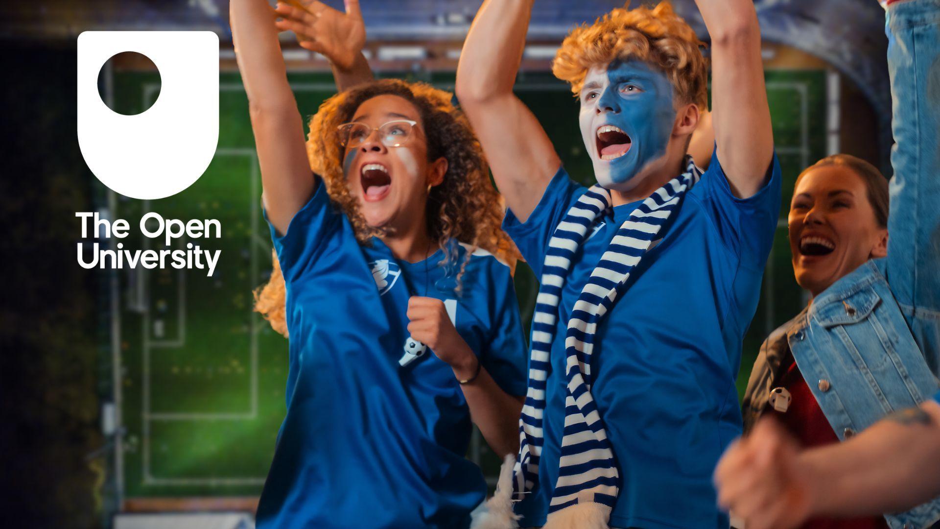 Two football fans cheer while wearing blue shirts and face paint.