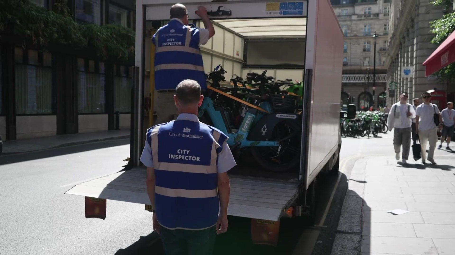 Two people load hire e-bikes into the back of a white van.