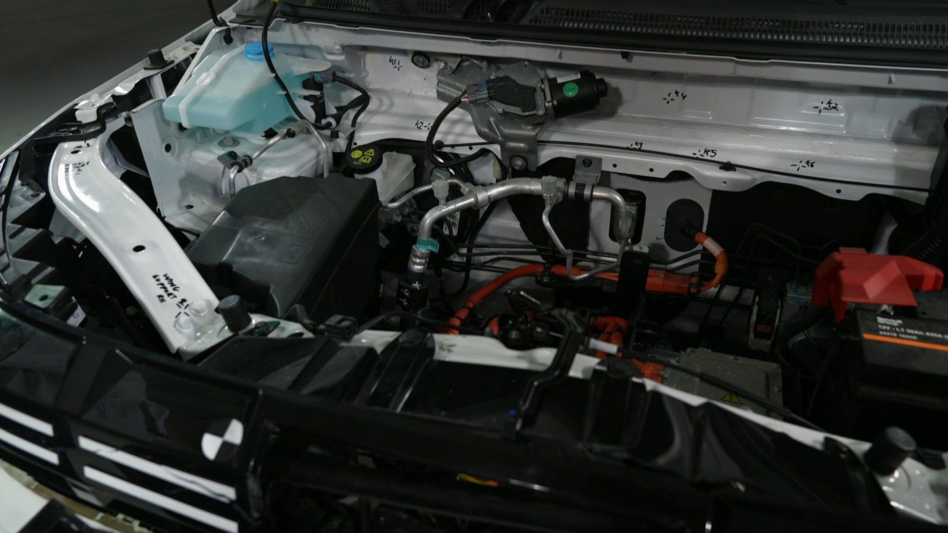 The inside of an EV under the bonnet. The components and the damage to them are not immediately obvious to a layperson. There are metal pipes, rods, wires, and plastic pieces of kit.