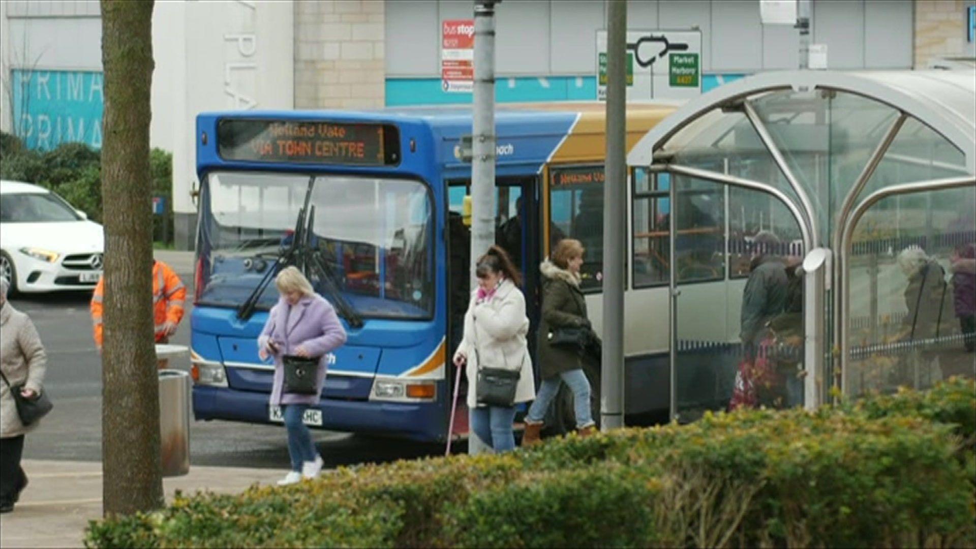 A bus is parked next to a bus stop with people exiting and waiting to board. 