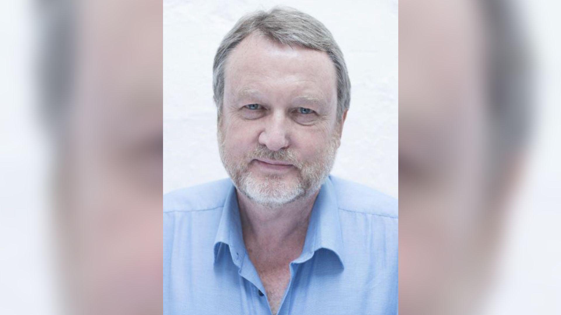 A man with a short beard smiling at the camera. He is wearing a blue shirt.