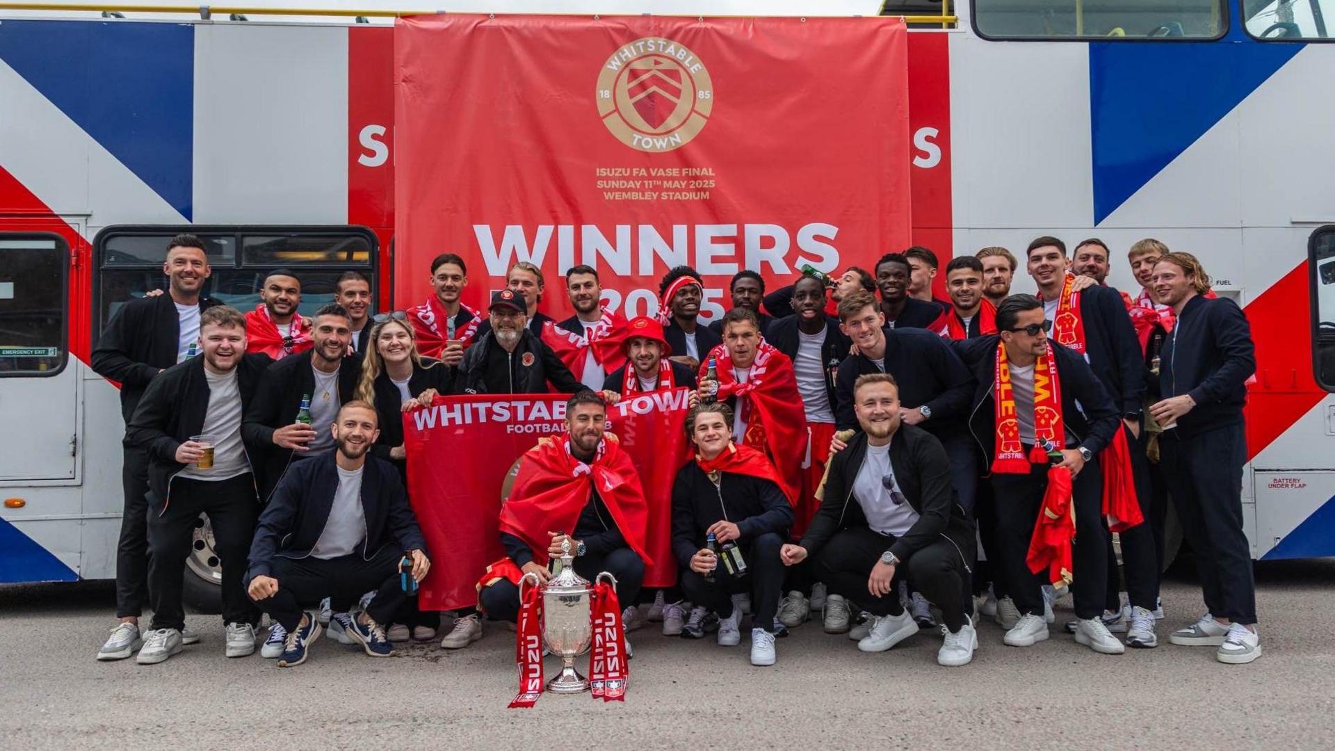 The team standing with the cup in front of the bus.