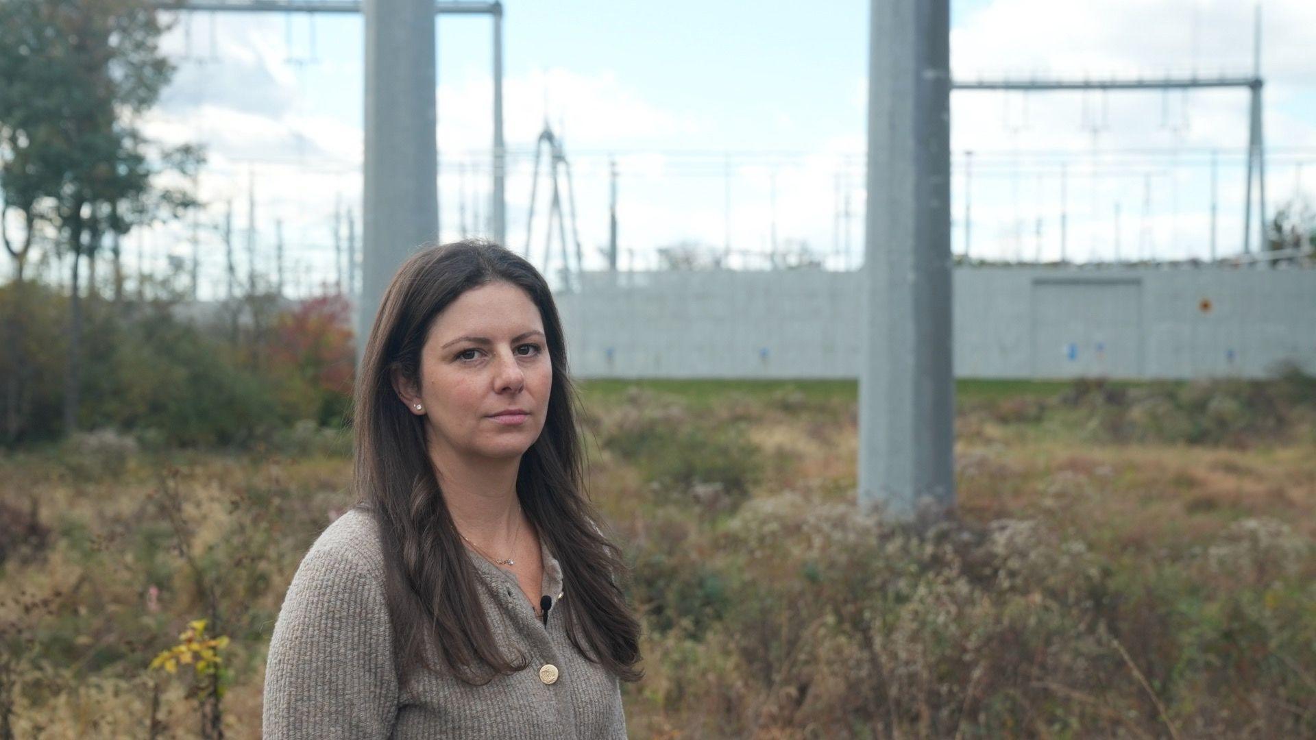 Emily Kasabian stands in front of a substation with giant poles.