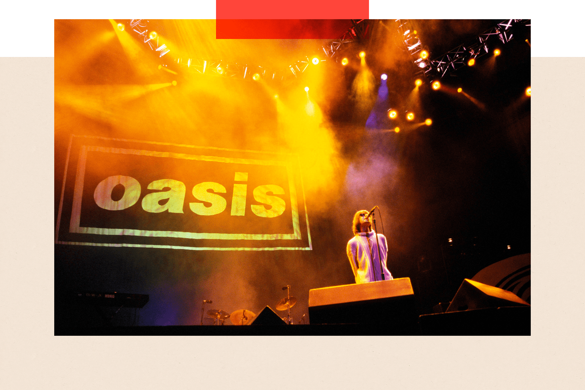 Liam Gallagher in a white coat singing in front of the Oasis logo