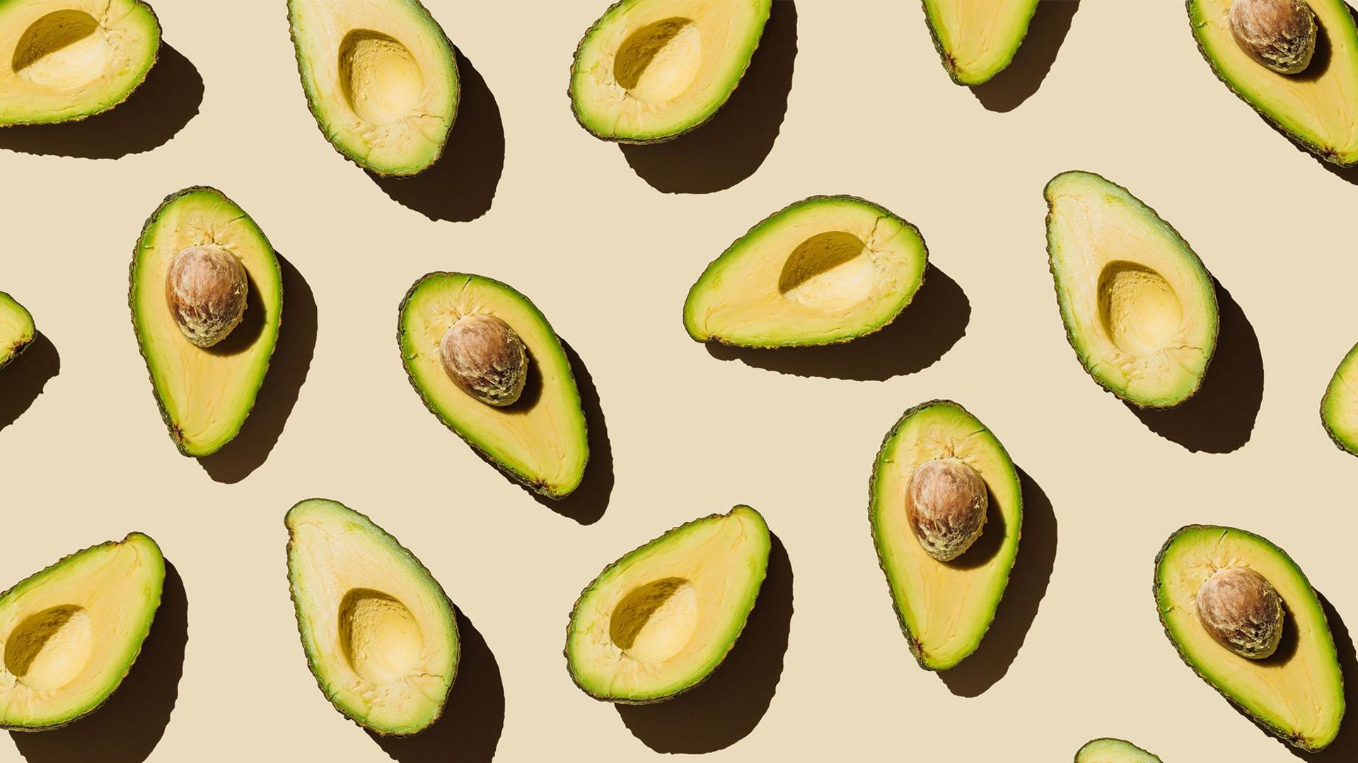 Halved avocados scattered on a beige surface with graphic shadows. 