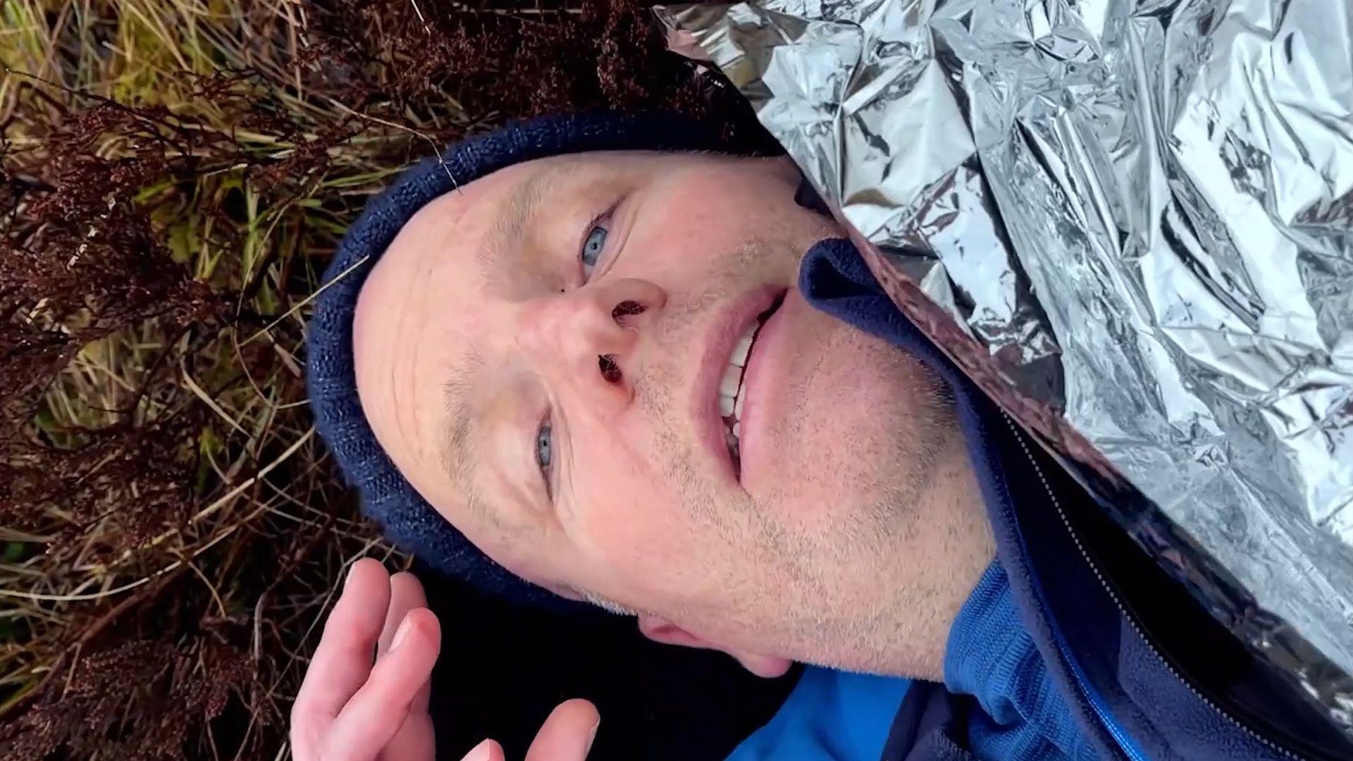 Glenn Campbell lying on the ground looking up at the camera, with a foil blanket over him.