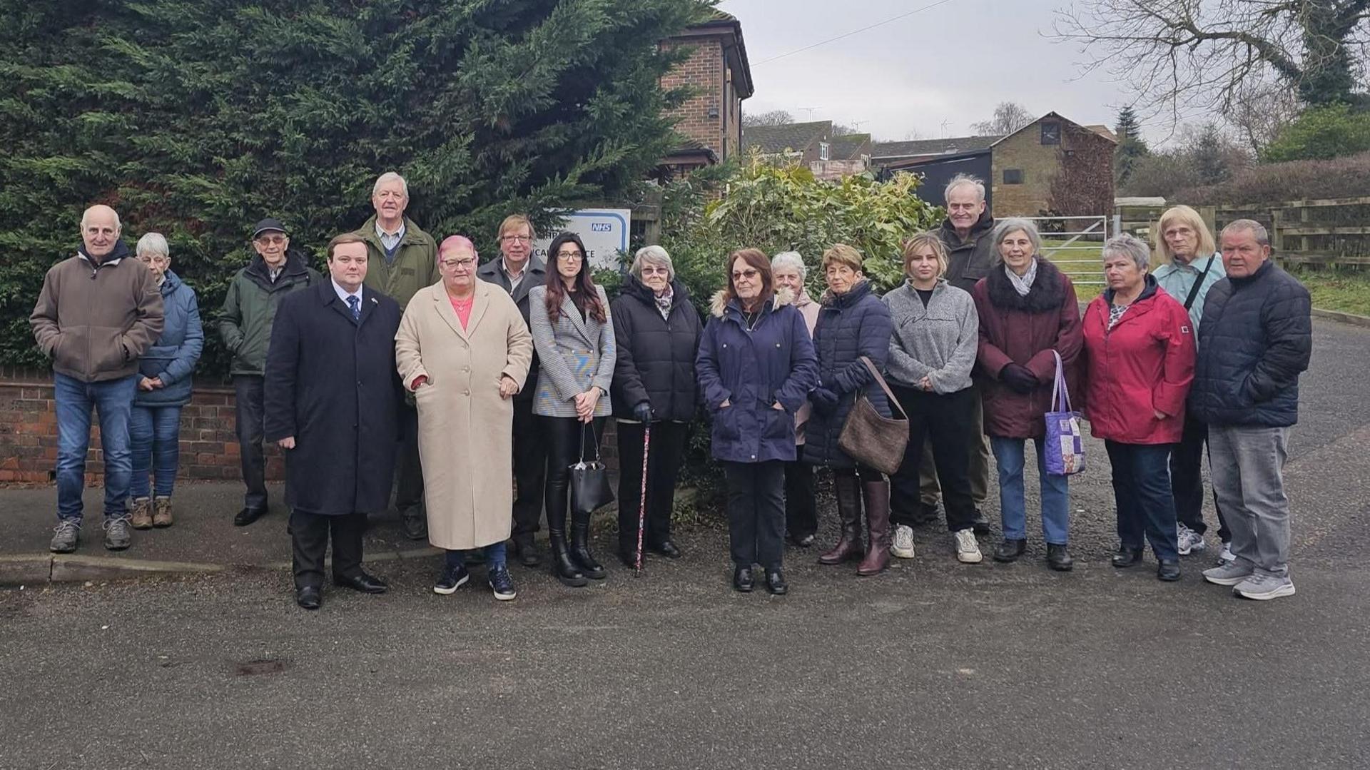 A group of eighteen people stand in front of a the GP surgery in Higham in Kent