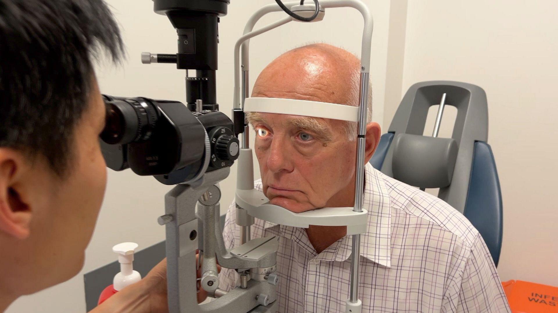 An optician looks into a man's eye using a machine