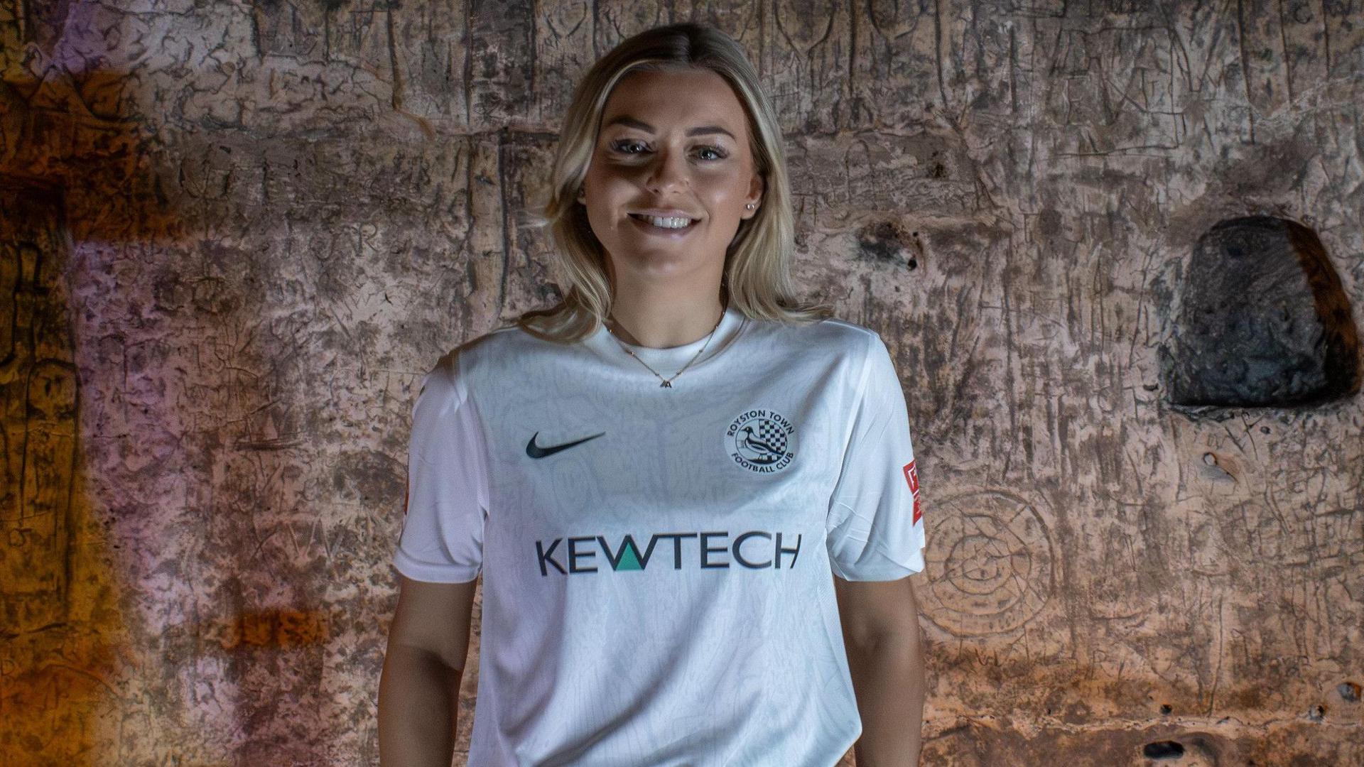 A female Royston Town FC player wearing a new football shirt, standing in Royston Cave, Hertfordshire