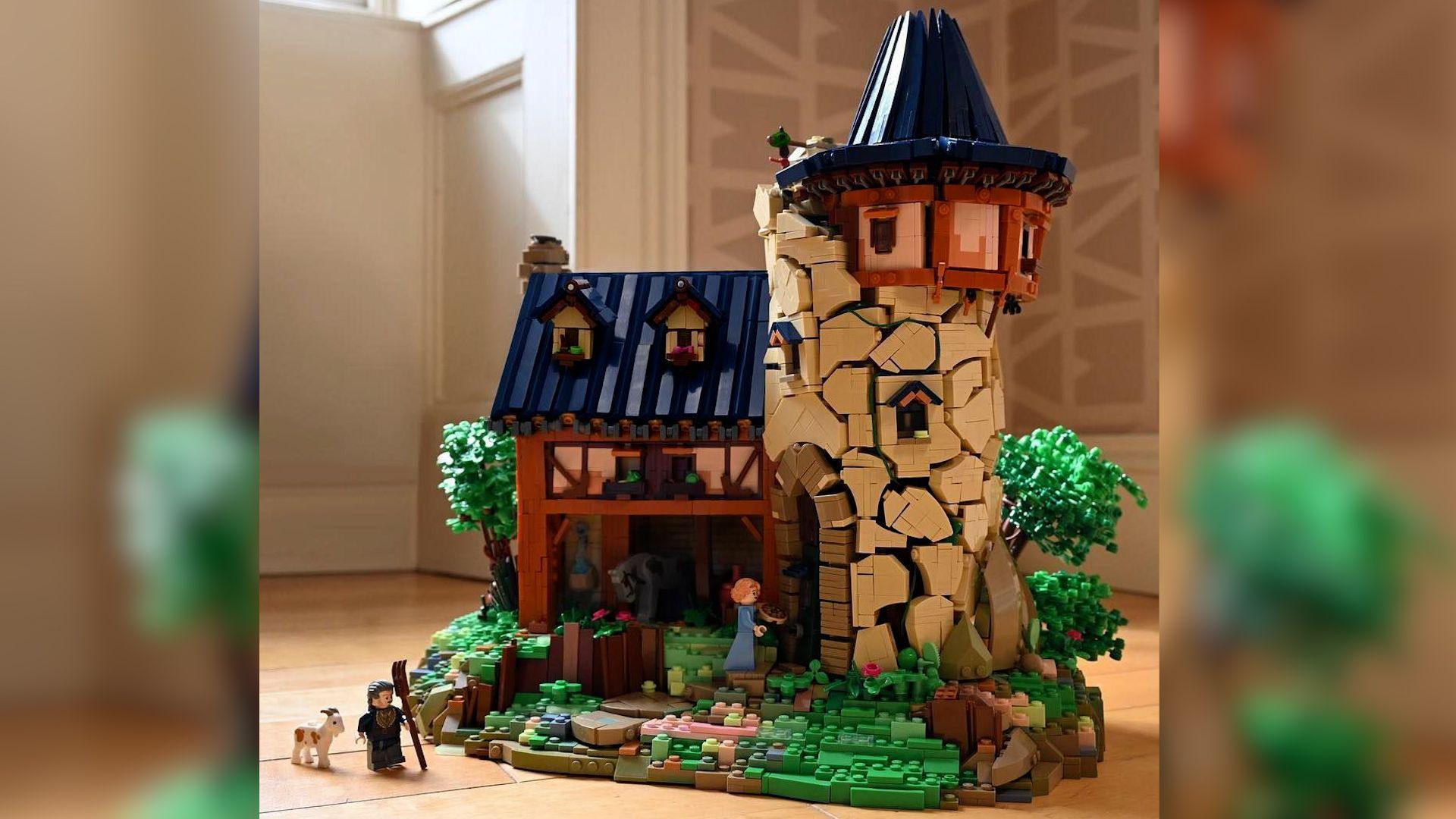 A lego model of an old tower with a blue roof attached to a cottage like building. There is a woman minifigure on a grassy slope at the door of the tower and a man with a pitchfork walks nearby with a tiny goat.