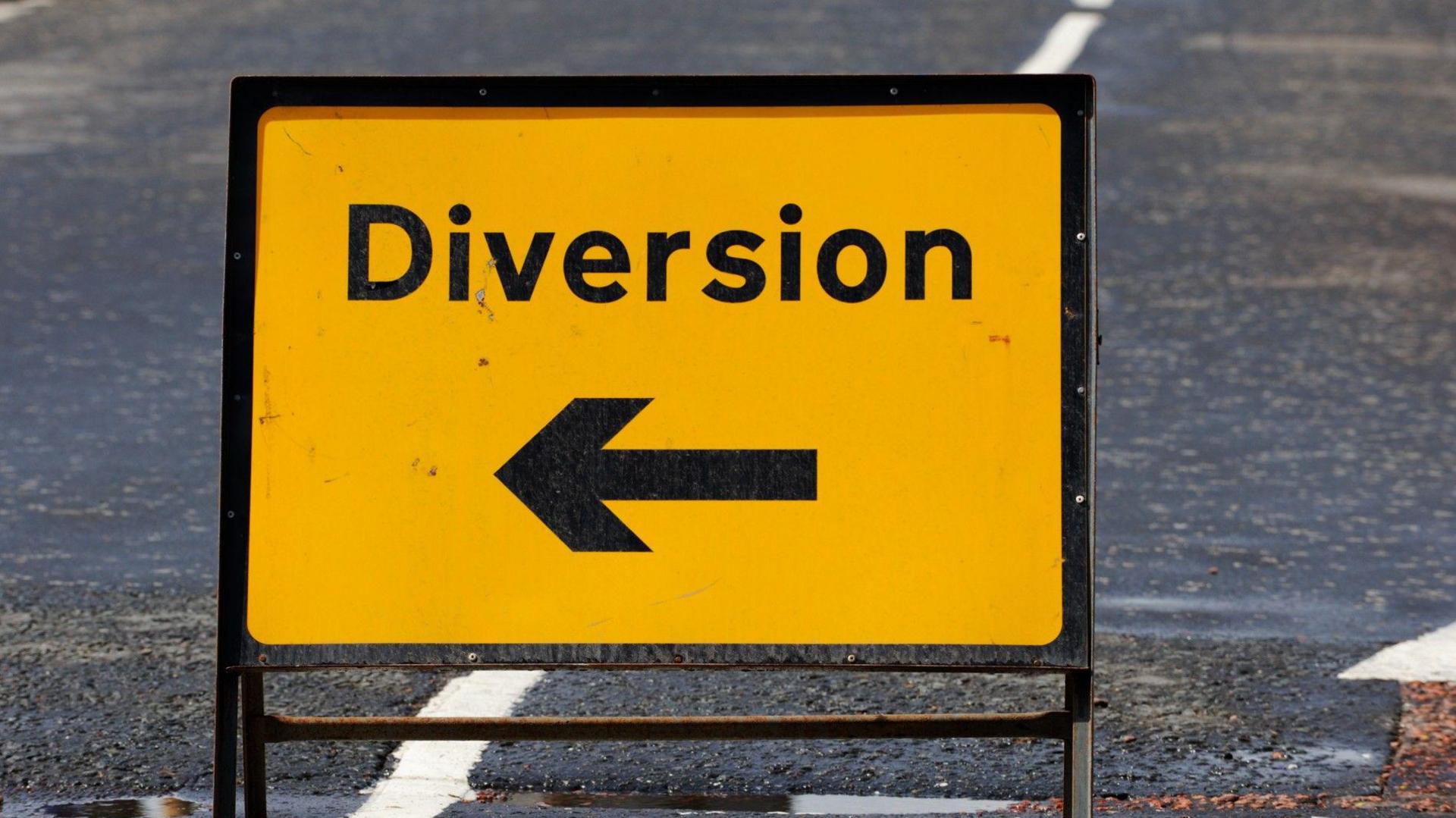 A yellow and black arrow diversion sign set up on an urban road.