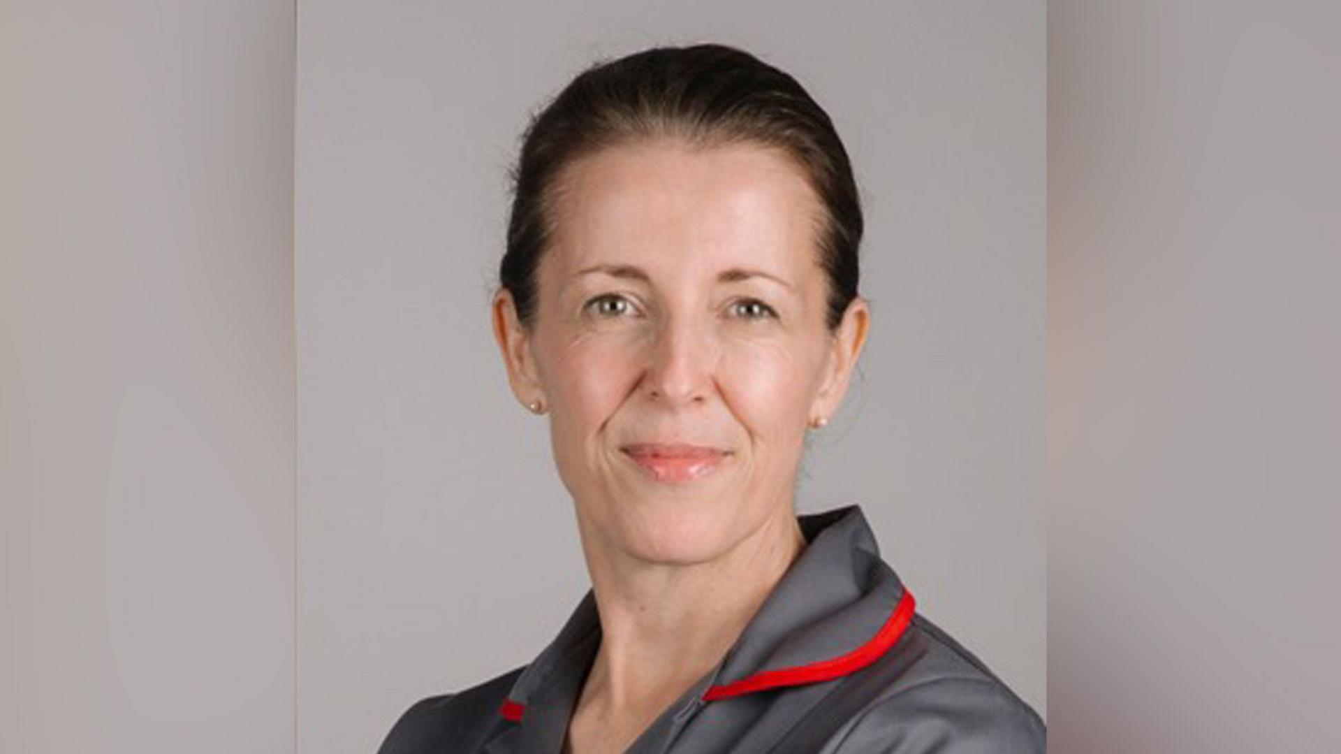 Sam Young smiling in a grey and red nurse outfit. She has brown hair tied into a bun.