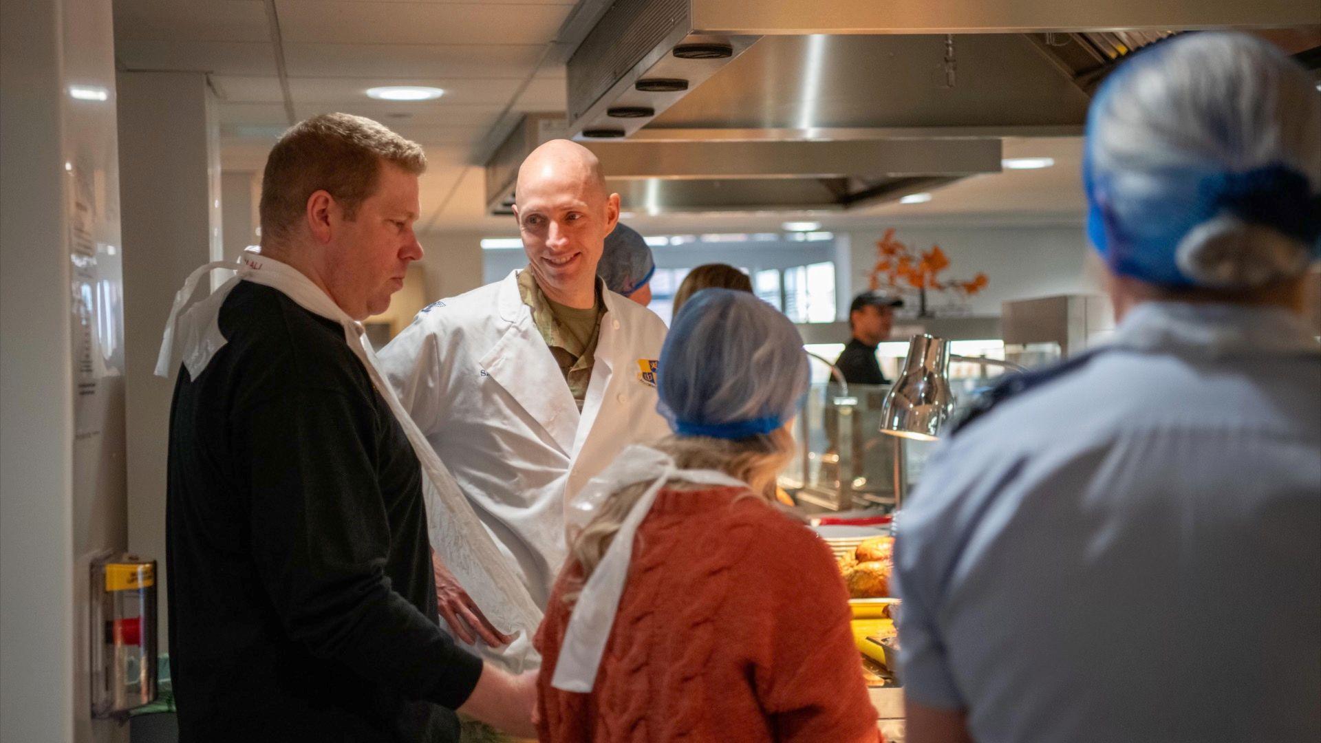 People smiling and chatting whilst cooking a Thanksgiving dinner for the Americans at RAF Fairford. 