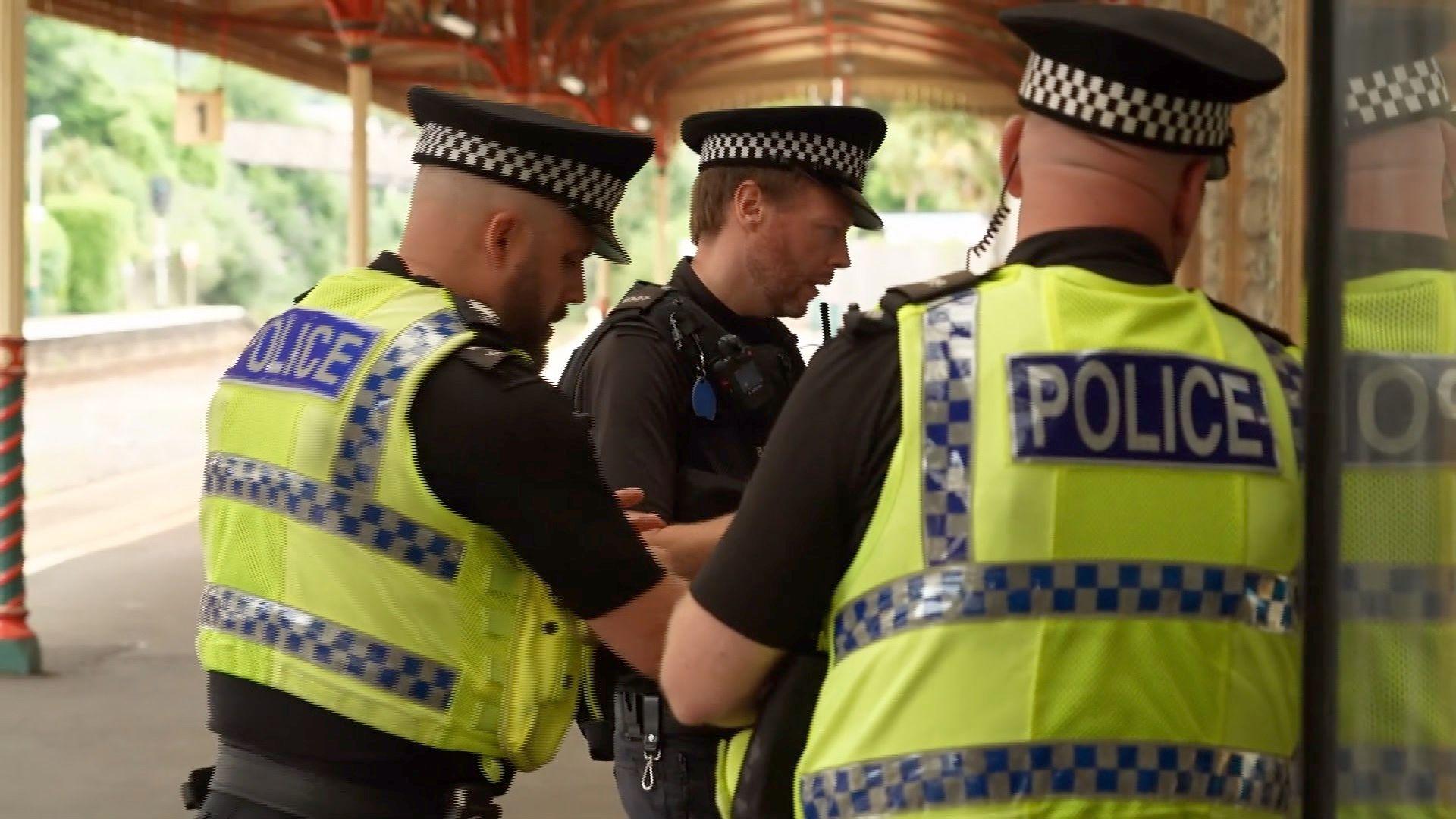 Three police officers at a train station. The officers are in police uniform. They are standing on a platform.