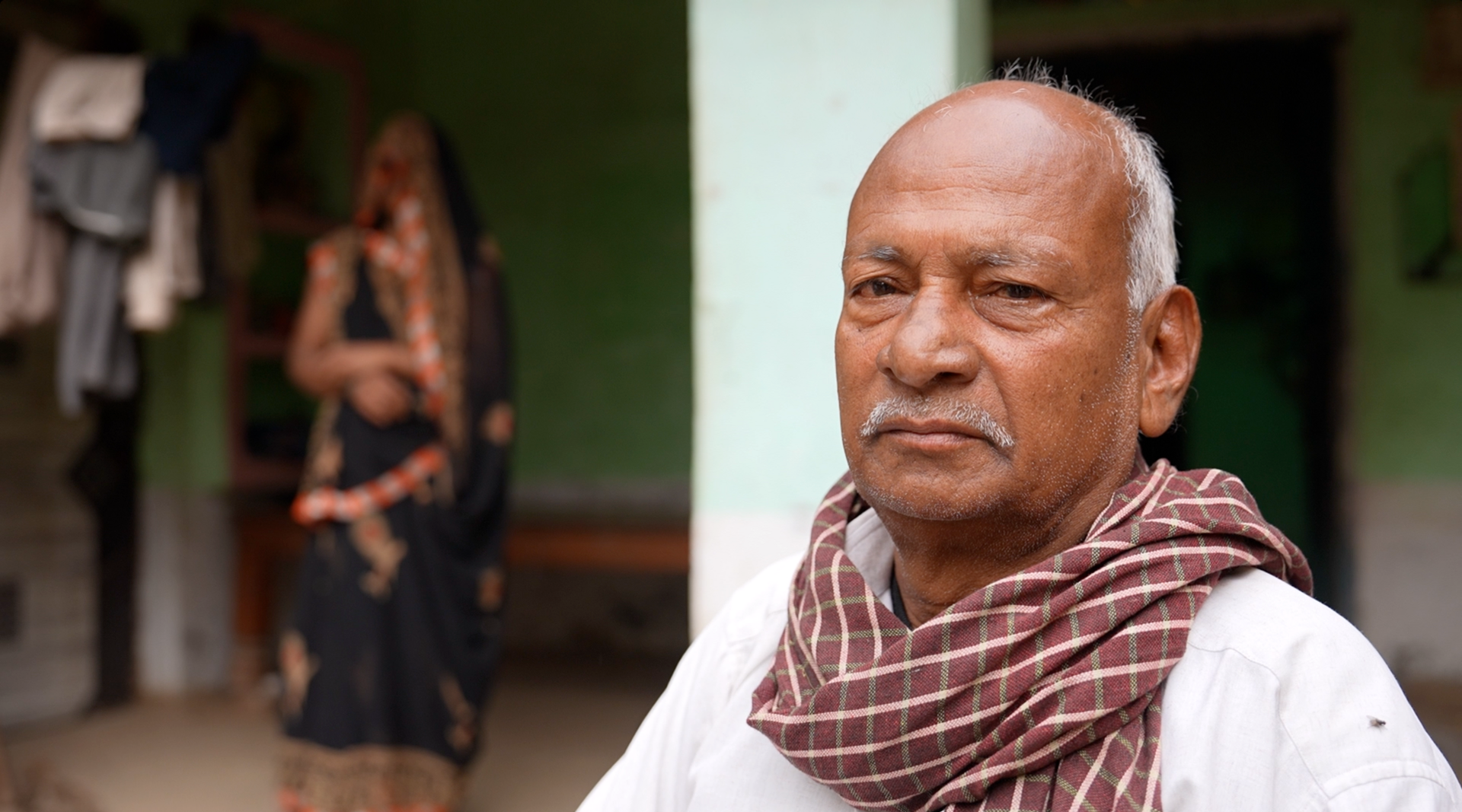 A man wearing a white shirt ad red checkered scarf looks into the camera