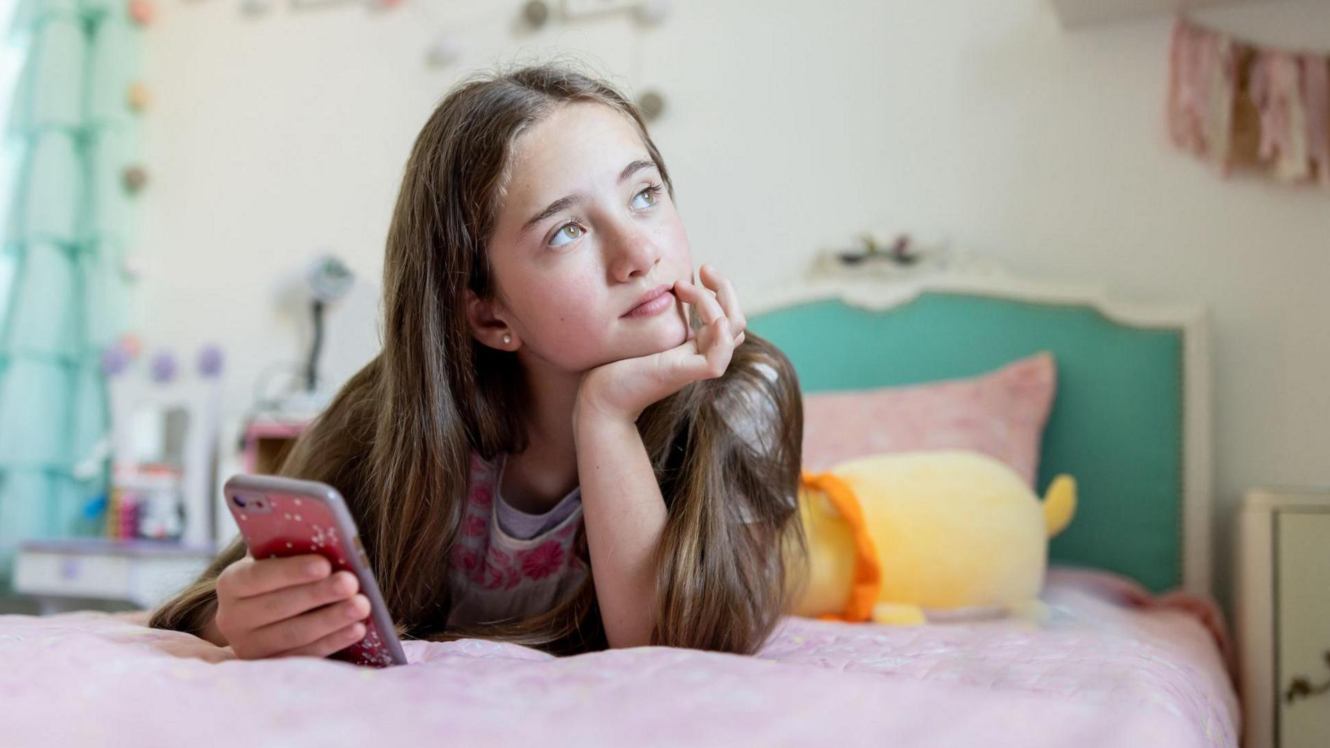 a teen girl looking thoughtfully up from her phone in her bedroom