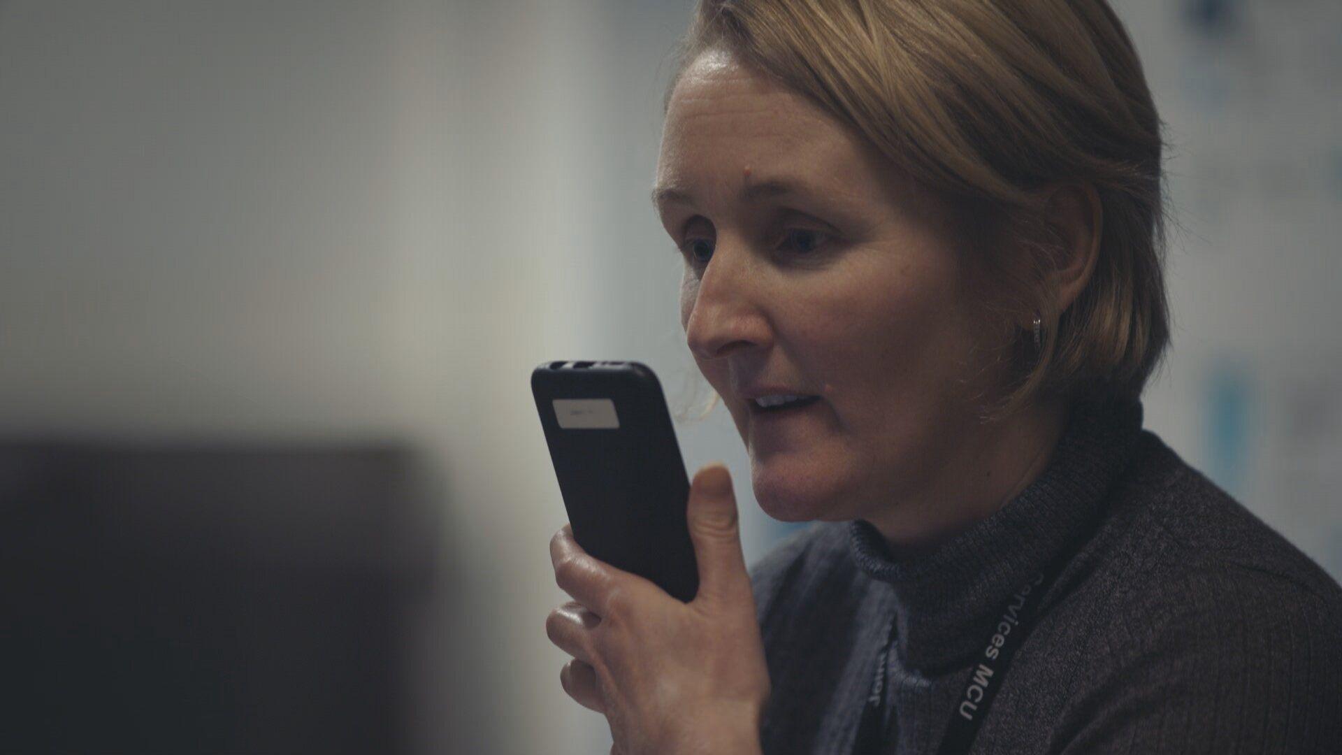 Woman with short blonde hair holding a mobile phone in front of her face