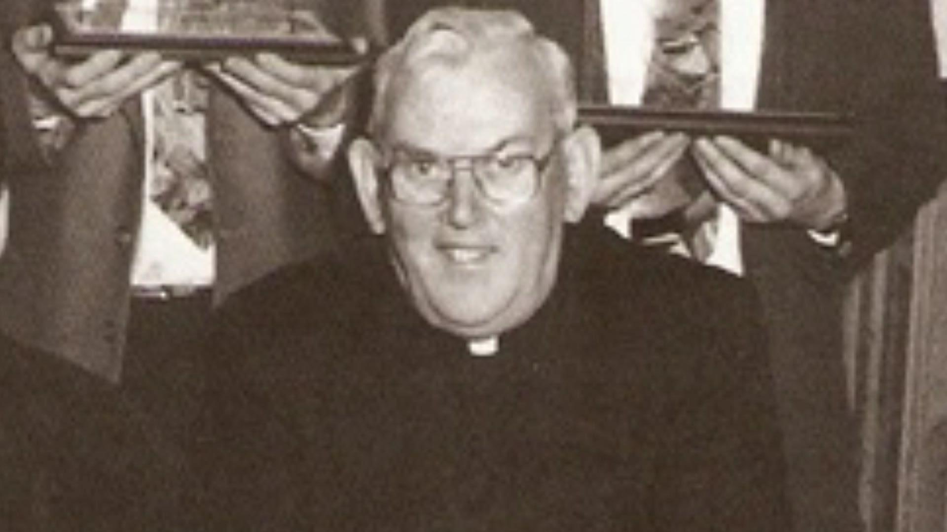 A black and white photo of the late Fr Malachy Finegan. The priest had short white hair and glasses and wore a black suit with a white clerical collar.