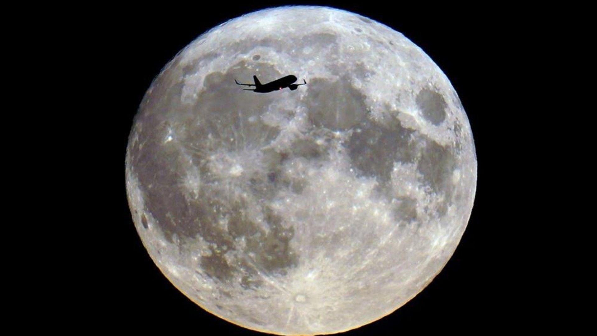 An aeroplane silhouetted across a bright full Moon in the night sky