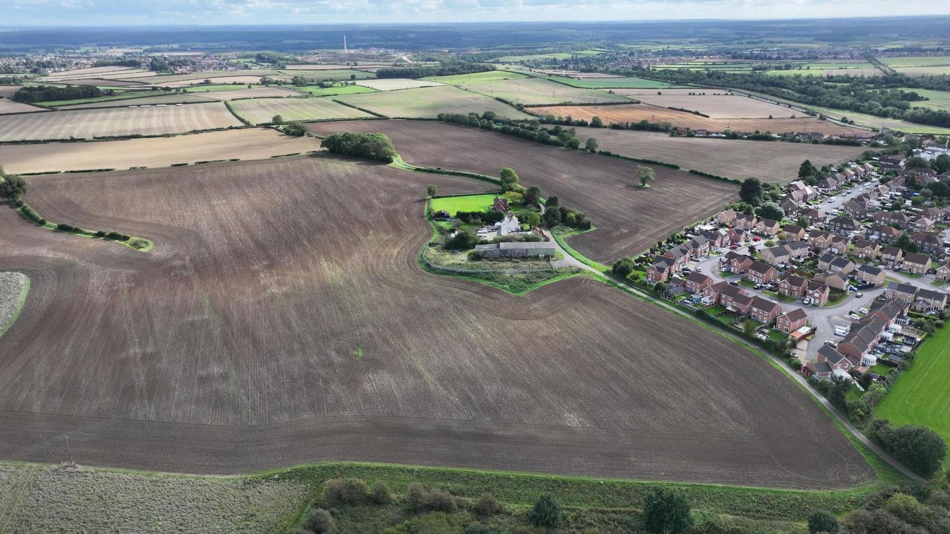 An aerial image of land that is set to be developed near Clowne. It is mostly brown fields, with homes to the right.