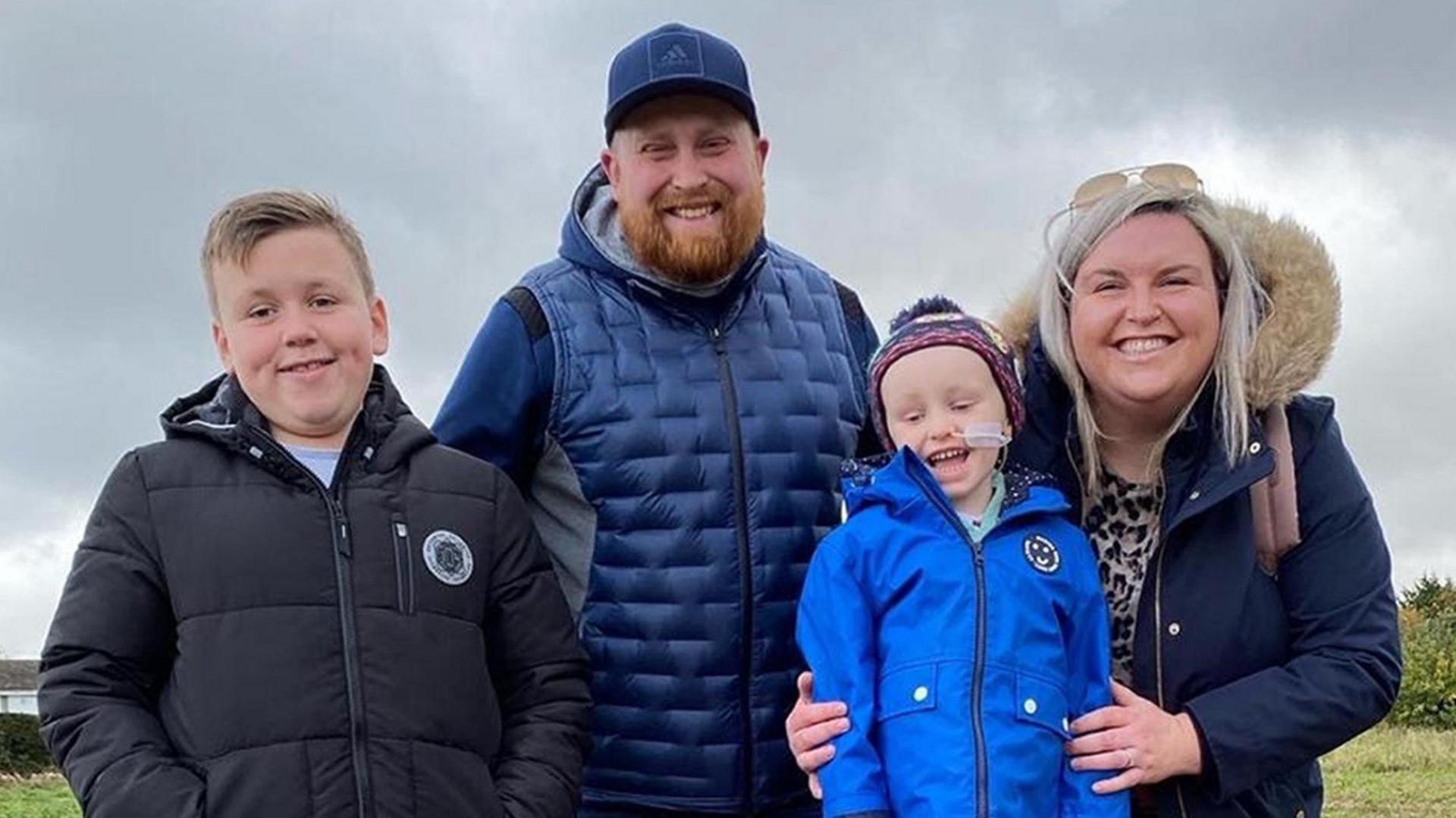 Luke and Karen Staples with Zac and his older brother Dylan (left). The family are all looking at the camera and smiling. They are in a field