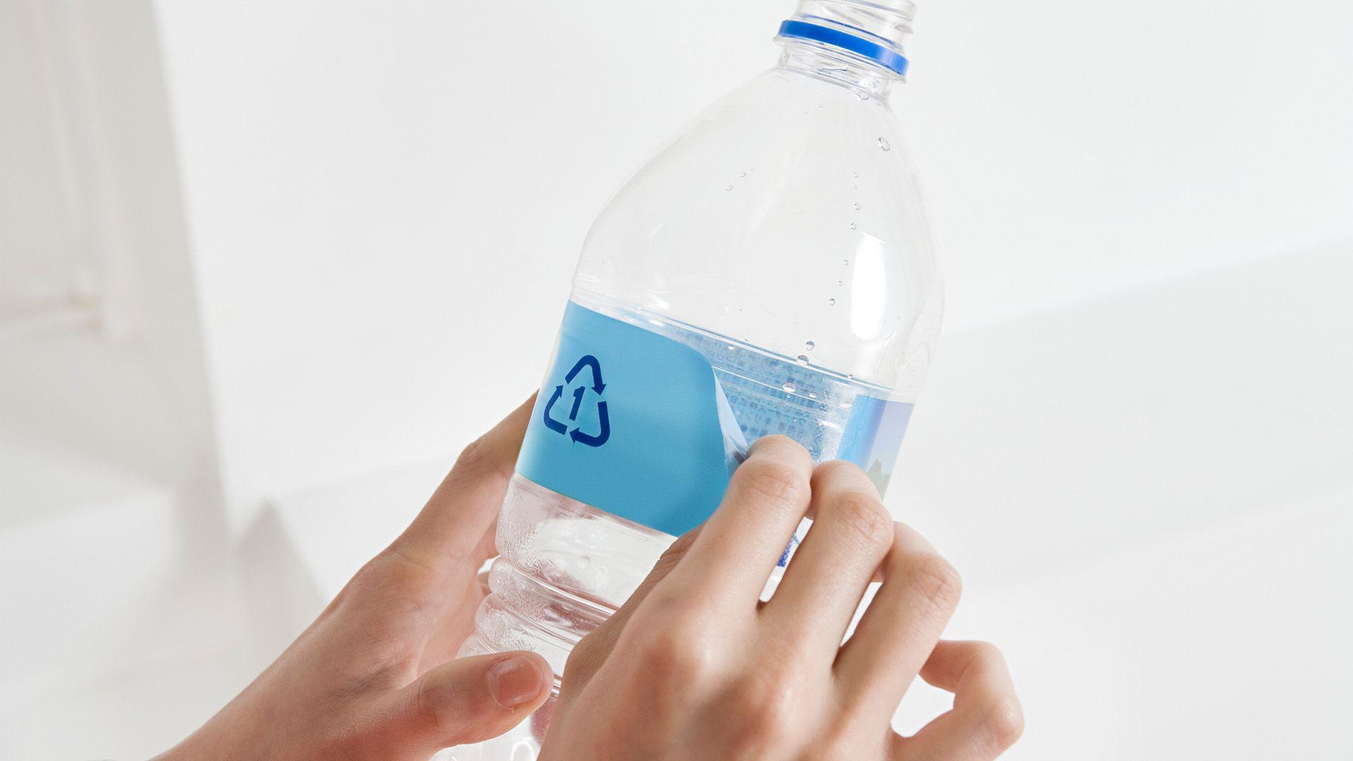 hand peels recycling label on plastic bottle