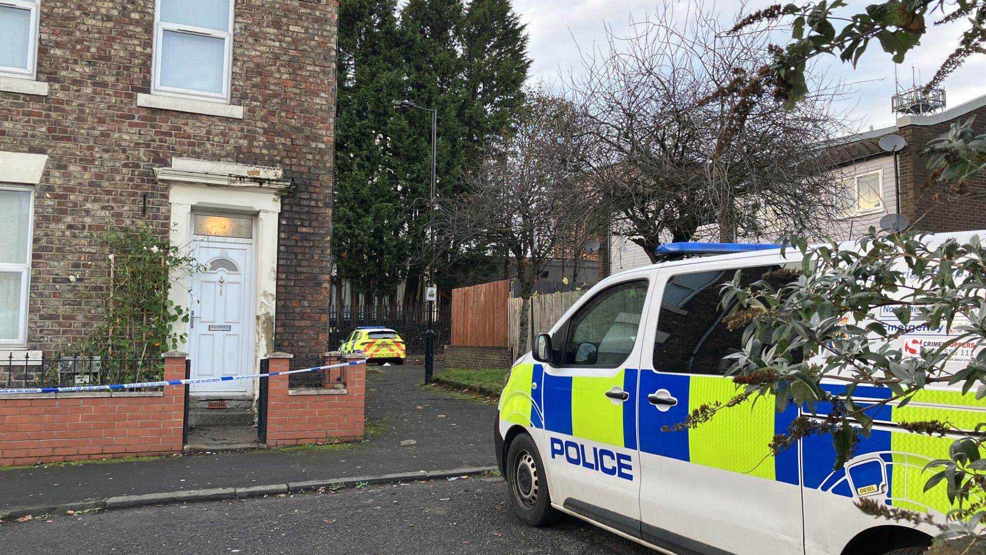 A picture of a police car outside a house with a white door. Police tape is around the property.