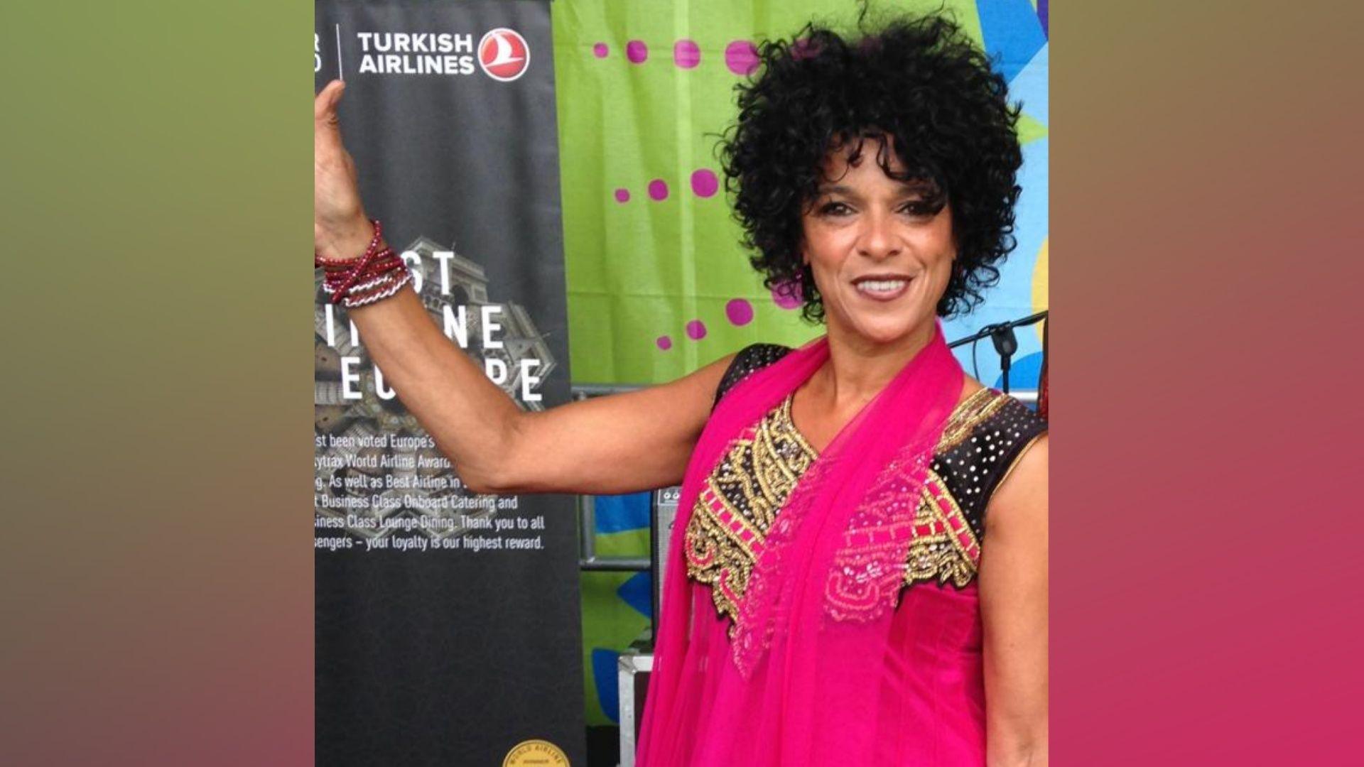 A woman, Carolyn Stewart at Belfast Mela. She has dark curly hair and is wearing a hot pink dress.
