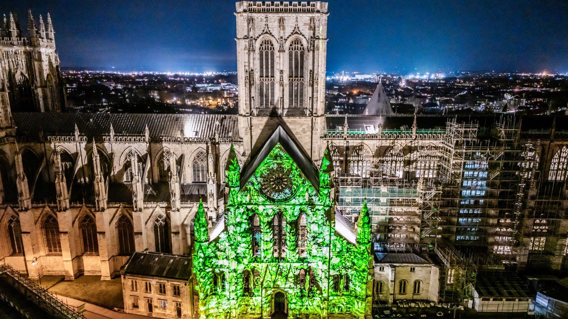 A wide image of York Minster at night, with a large projection of green light on one side of the building.
