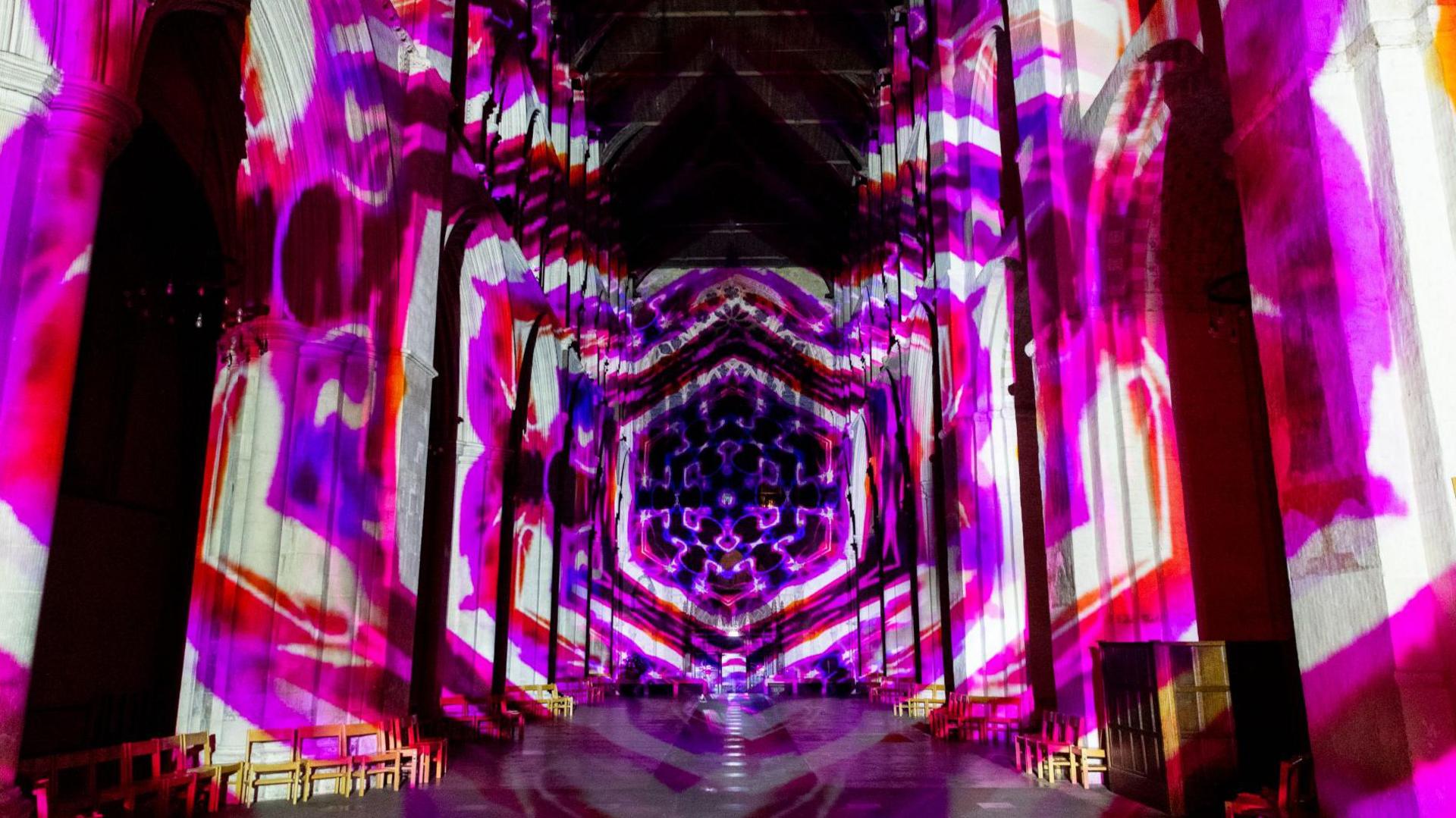 Larger poppy shapes in red, pink and purple are projected on to the walls and ceiling of the nave of St Albans Cathedral.