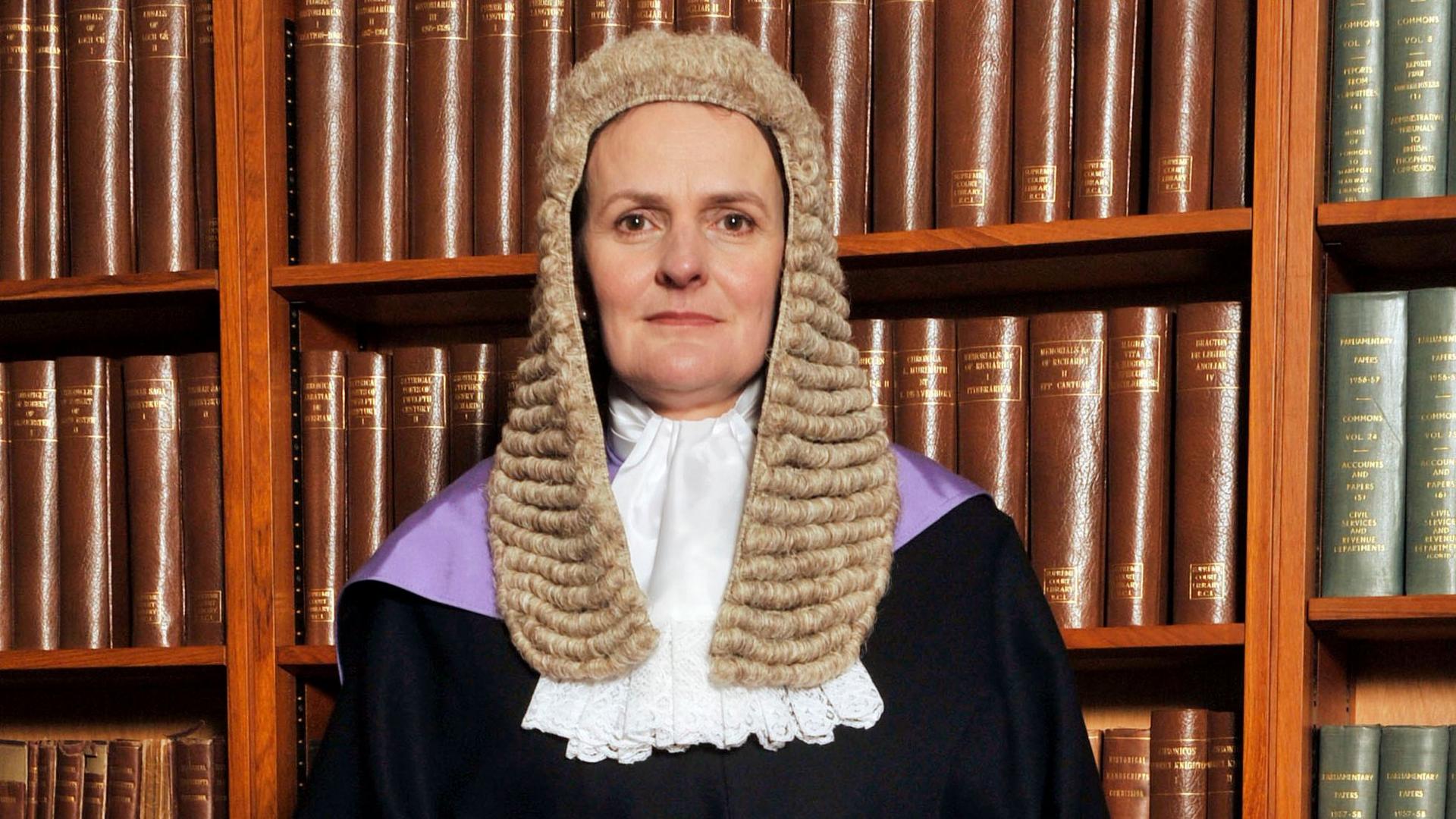 Judge Alison Raeside looks straight at the camera. She is wearing a wig and gown and is pictured in front of a bookshelf