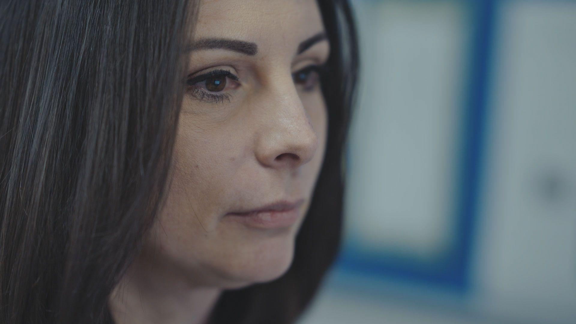 A close up shot of Katie, side on. She is looking slightly downwards with a serious expression and has straight dark hair and tailored eyebrows.