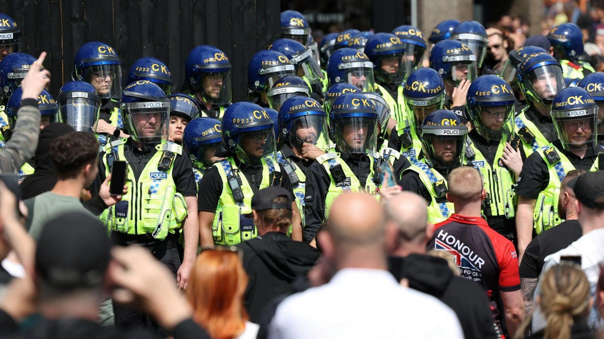 A line of police officers with riot helmets face a group of anti-immigration rioters in Manchester 