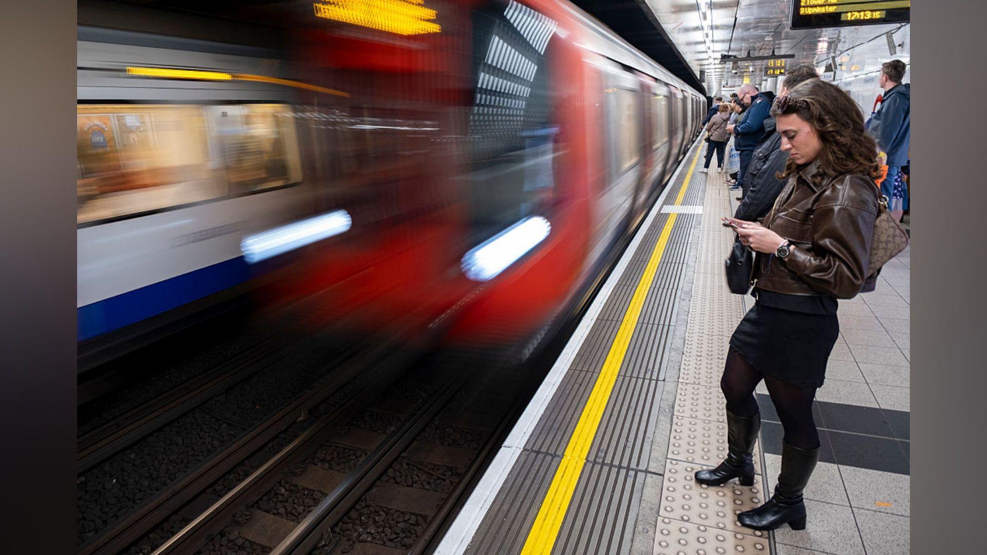 A blurred image of a Tube train pulling into a platform as people wait for its arrival.