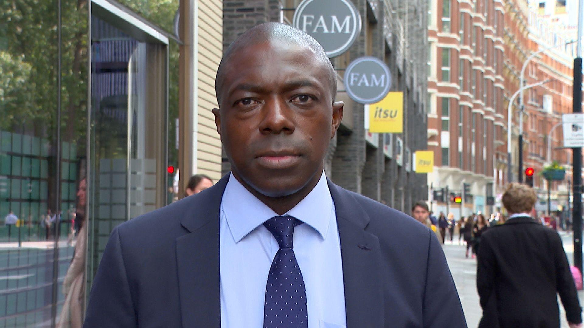 Bayo Alaba standing on the street in London and wearing a navy blue suit and tie 